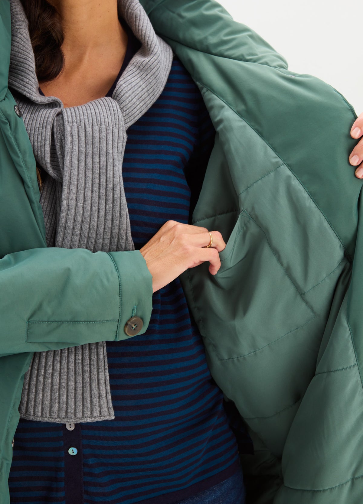 Open teal-green coat with a smooth finish, revealing a gray ribbed scarf and striped top underneath.