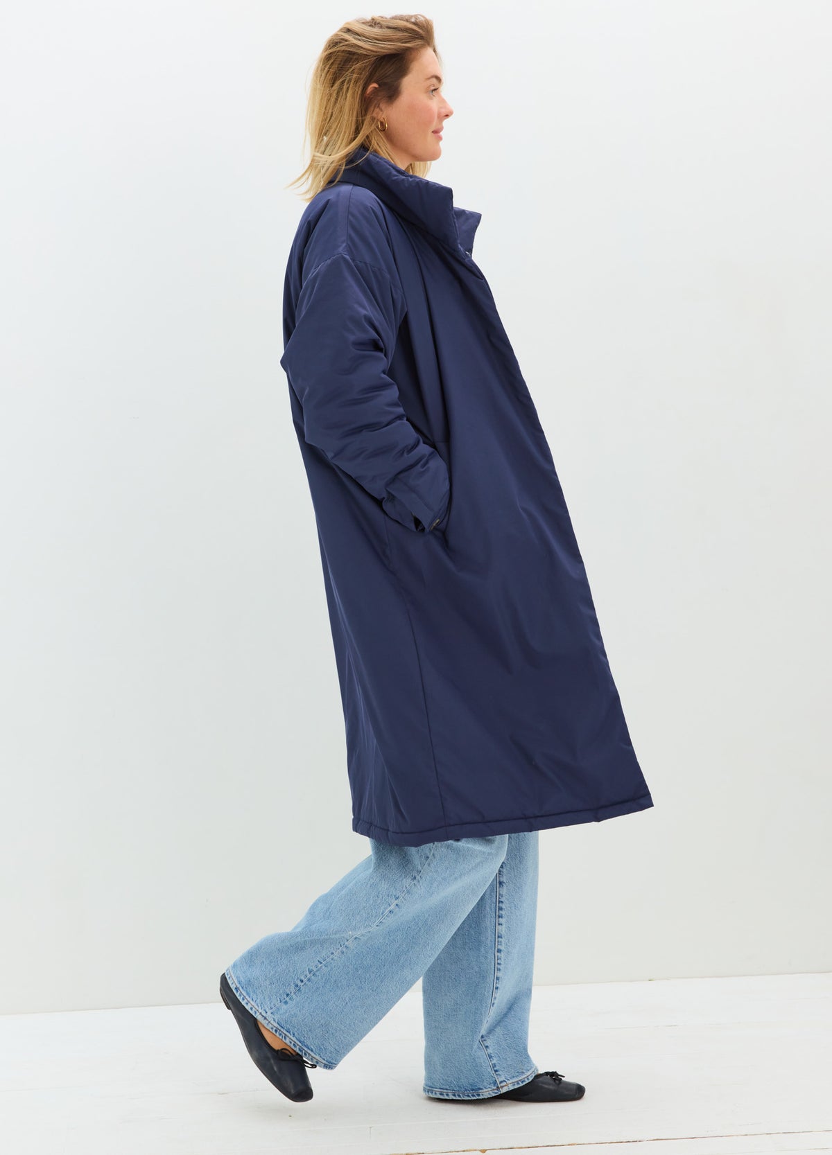 Long navy coat with a relaxed fit, wide lapels, and deep pockets, worn over light blue jeans.