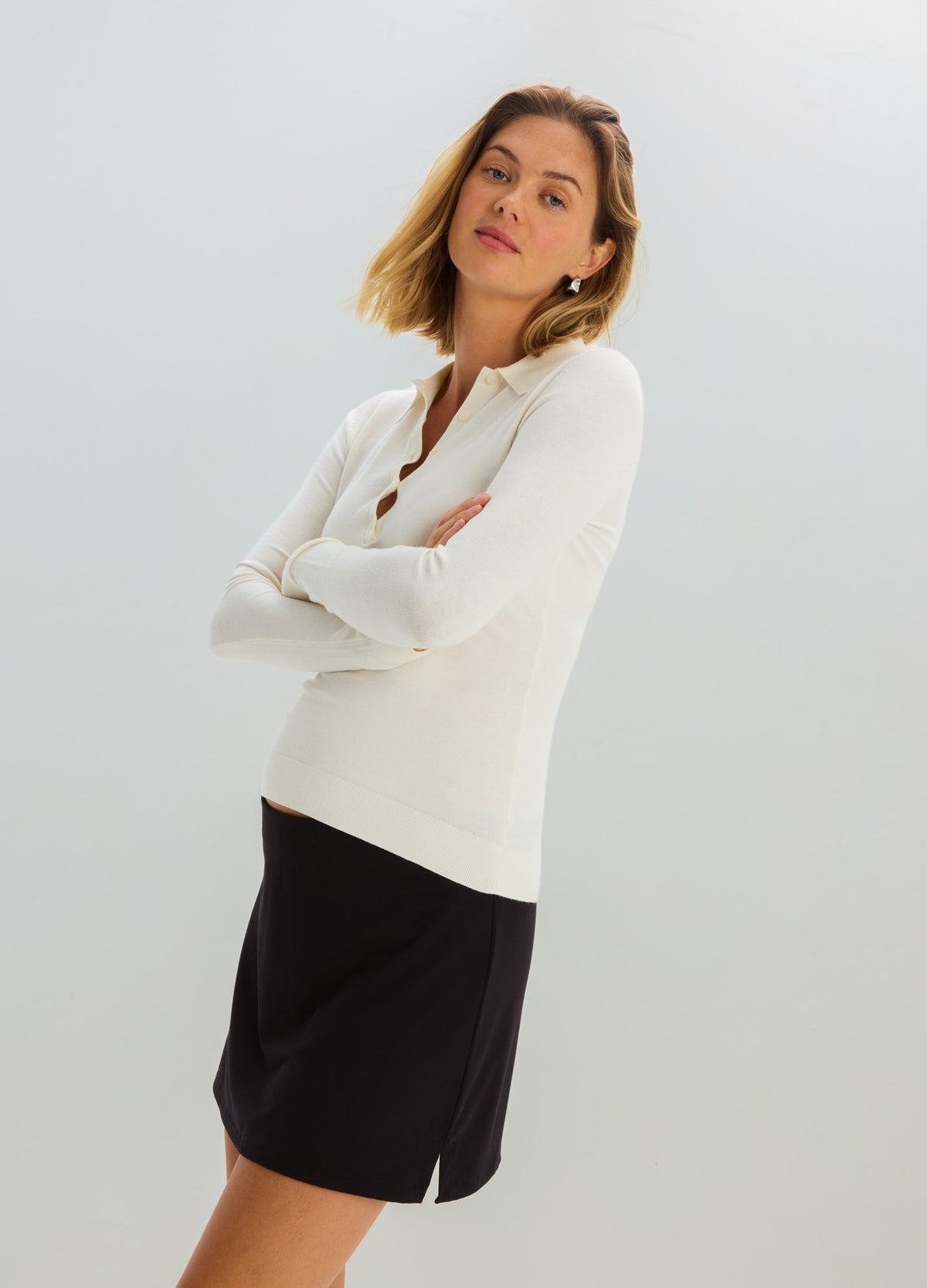 Cream-colored knit nursing polo with long sleeves and a fitted silhouette paired with a black knee-length skirt.