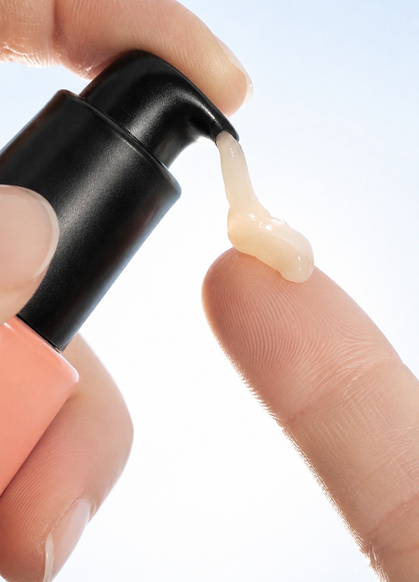 Clear beige balm being dispensed from a black pump bottle onto a fingertip.