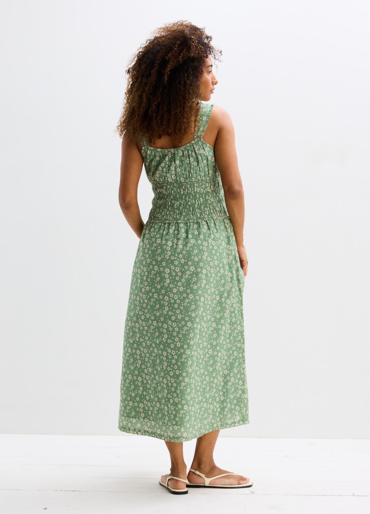 Green midi maternity dress with white floral print, smocked bodice, and adjustable shoulder straps.