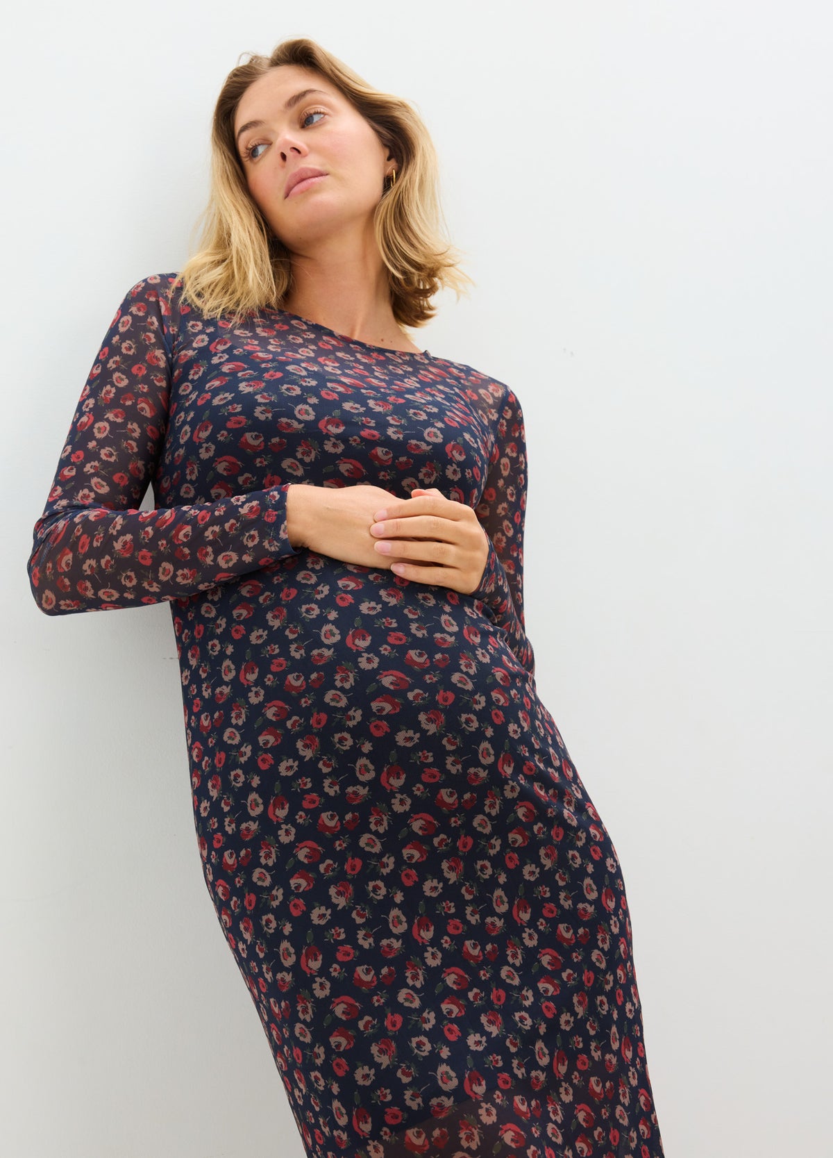 Navy blue maternity dress with red floral print, long sleeves, and a fitted silhouette over the belly.
