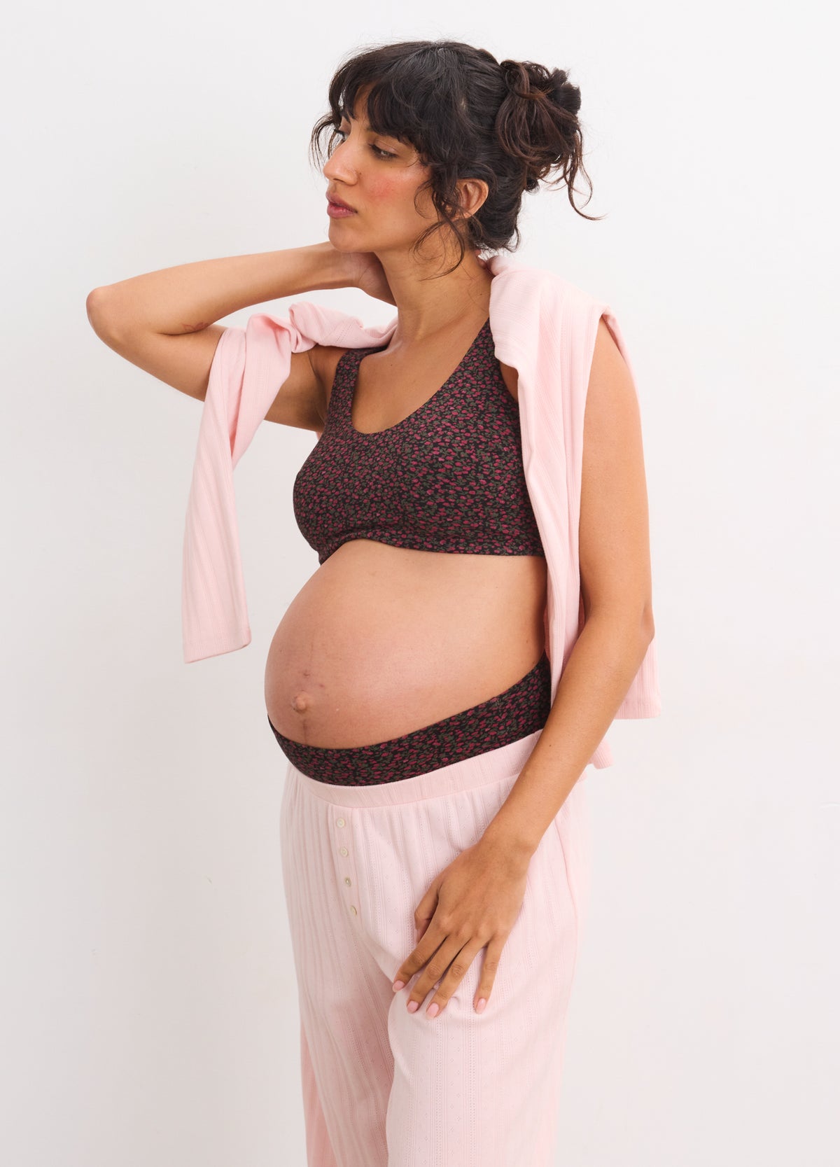 Black maternity bra with adjustable straps and soft fabric on pregnant woman wearing light pink pants and sweater draped on.