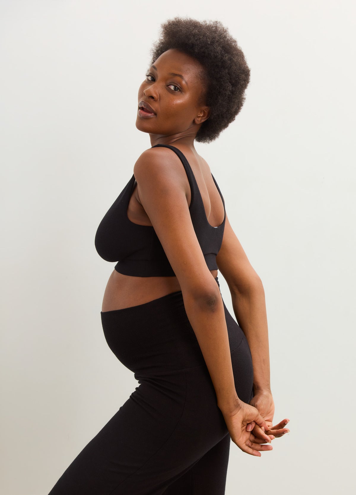 Pregnant model wearing a black ribbed maternity nursing bra and high-waisted leggings.