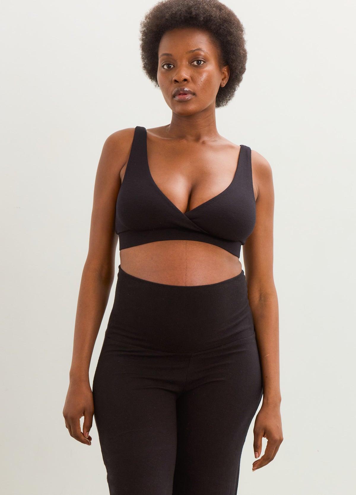 Black ribbed maternity nursing bra with wide straps and a supportive under-bust band, modeled with matching leggings.