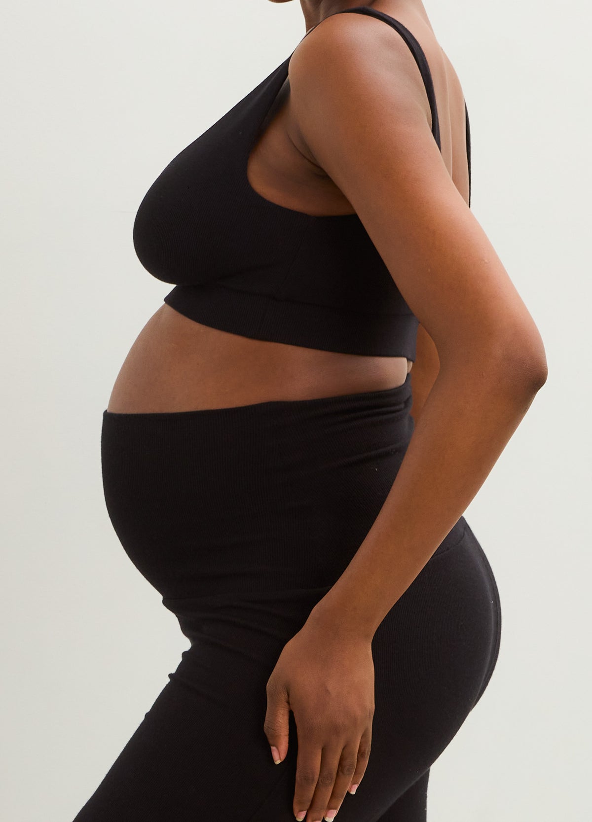 Black ribbed maternity nursing bra with thin straps, shown on a pregnant model from the side.
