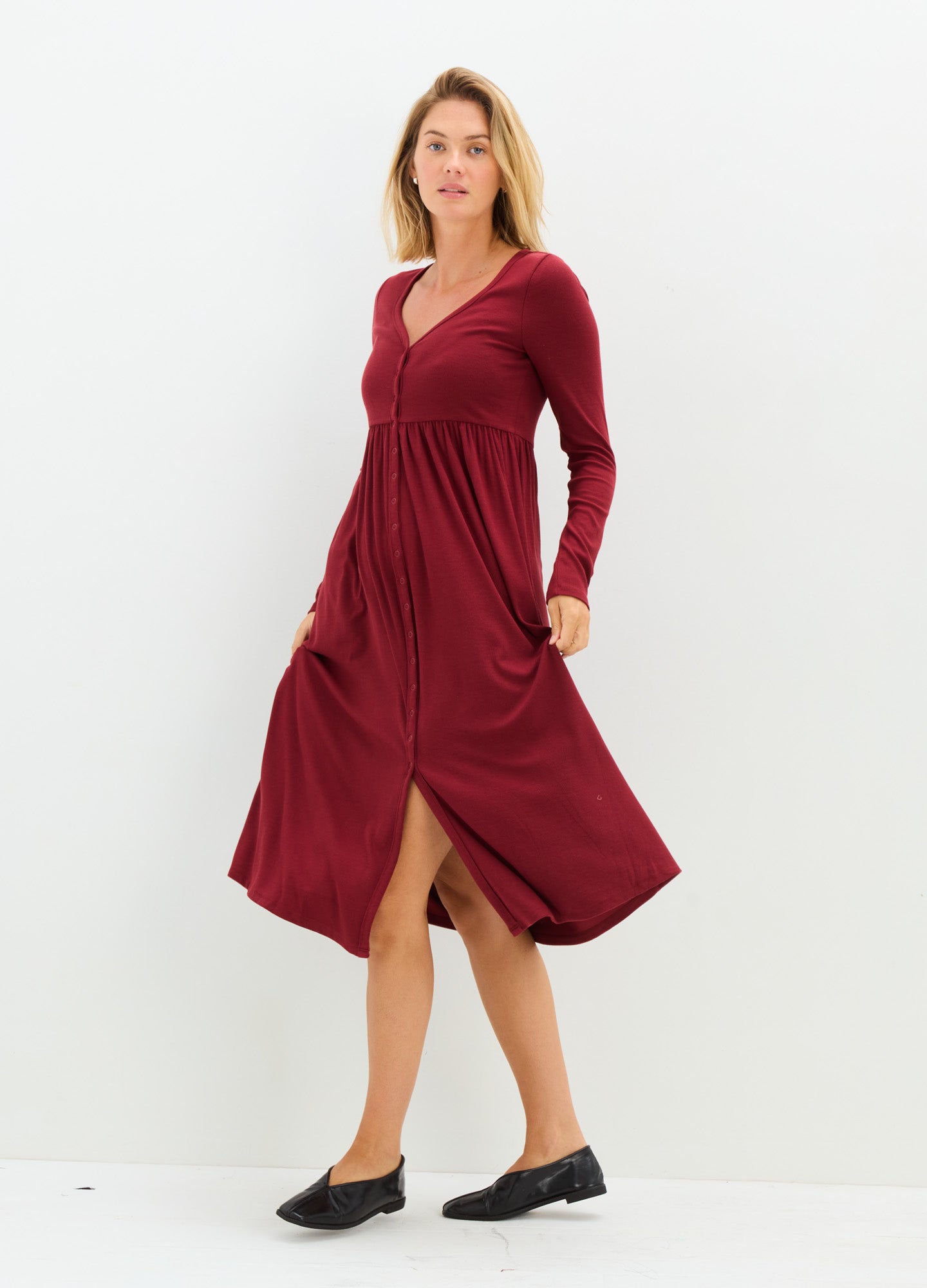 Burgundy long-sleeve ribbed maternity dress with V-neck and front slit, soft stretch fabric.