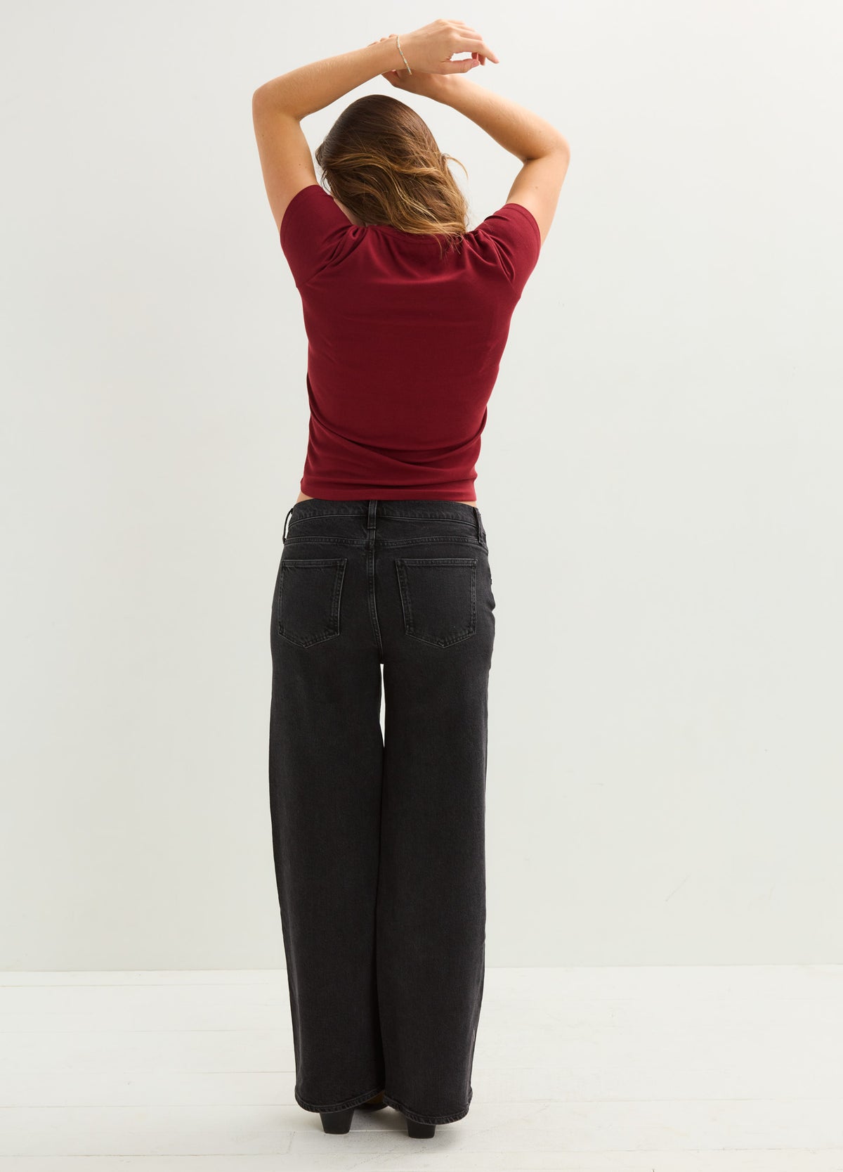 Soft ribbed maternity tee in deep red with short sleeves, fitted silhouette, worn with high-waisted black wide-leg jeans.