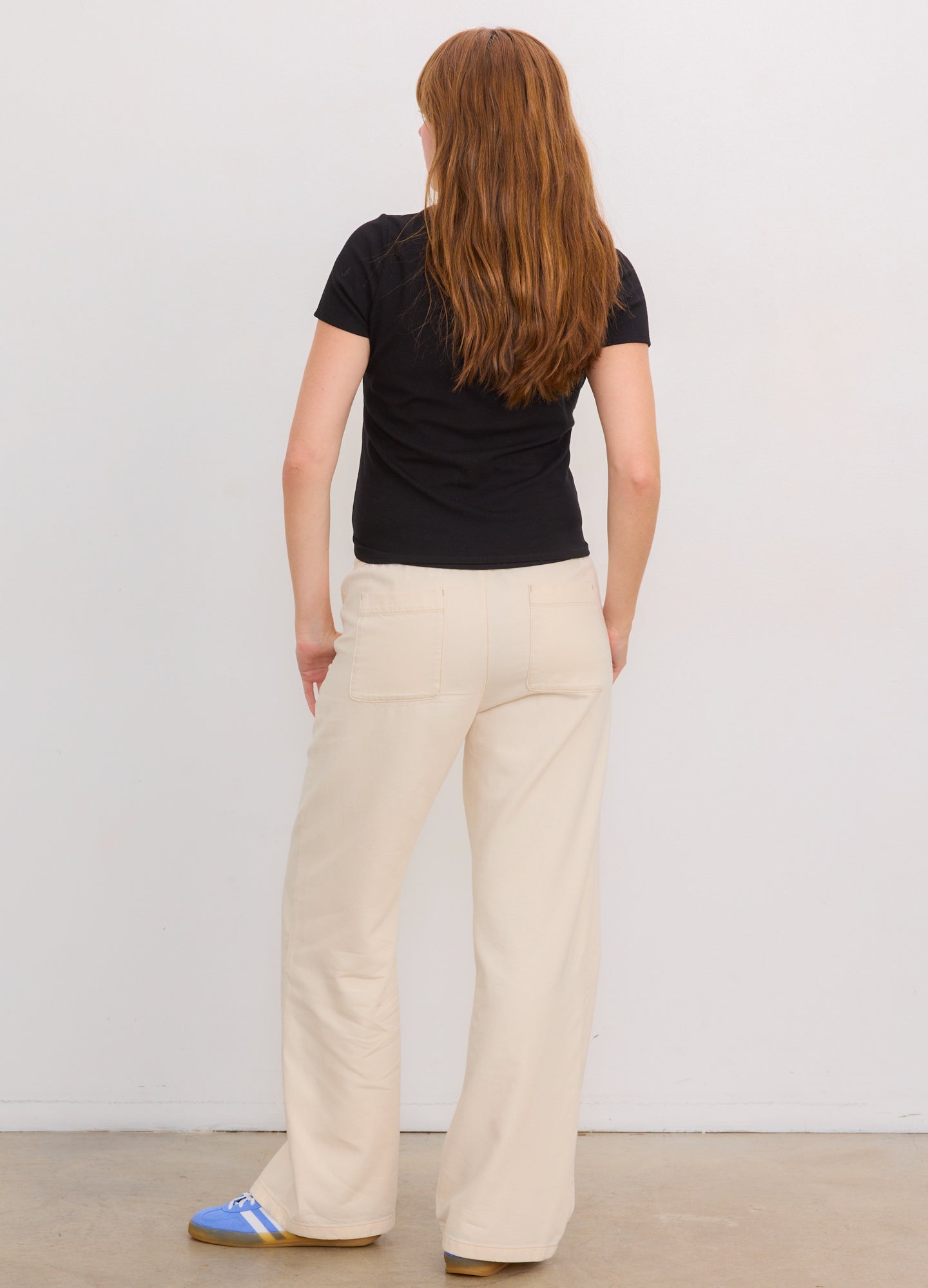 Black ribbed short-sleeve maternity tee paired with loose cream-colored pants and blue slippers.