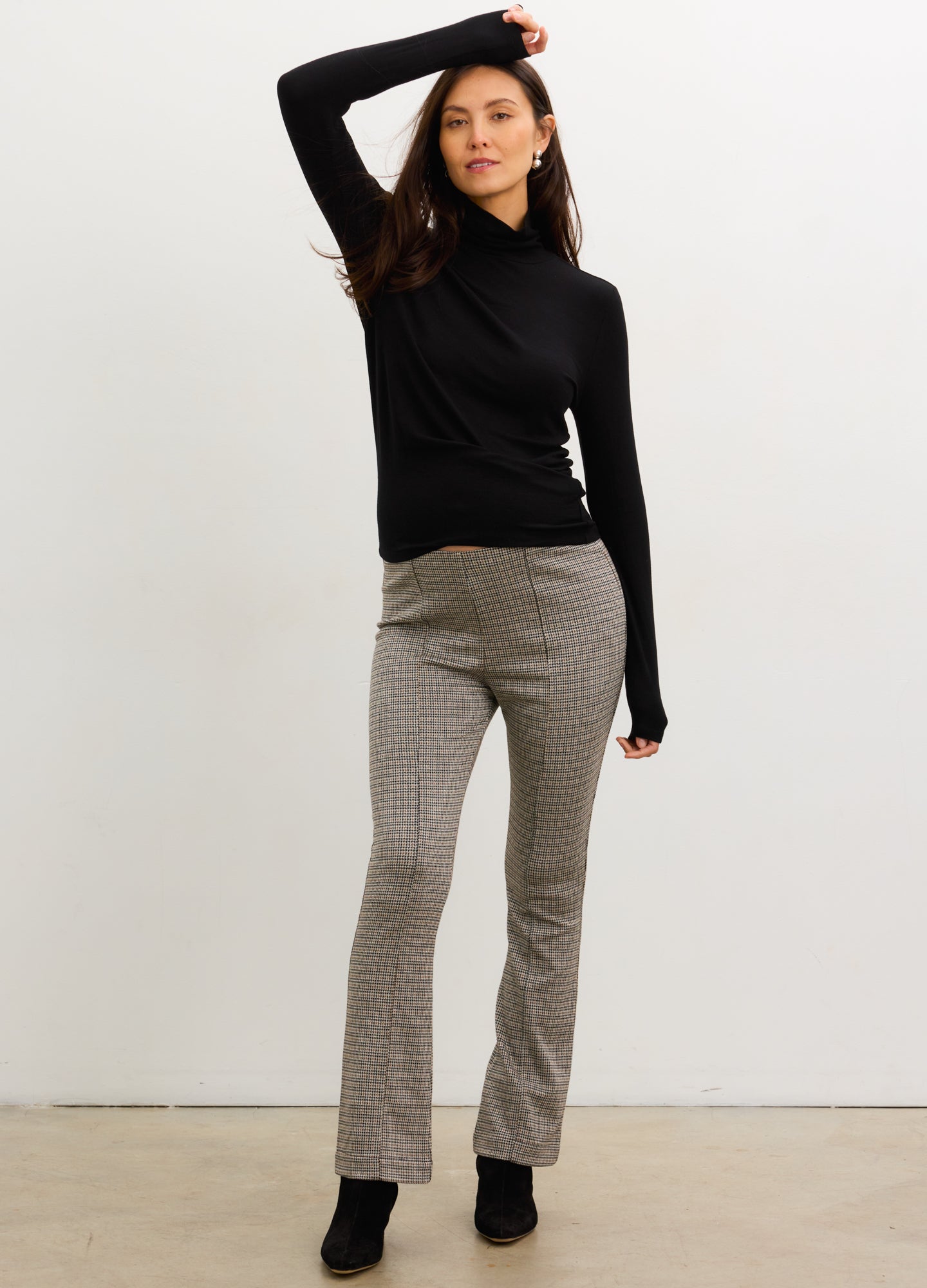 Pregnant woman wearing a black turtleneck and gray checkered pants against a white background