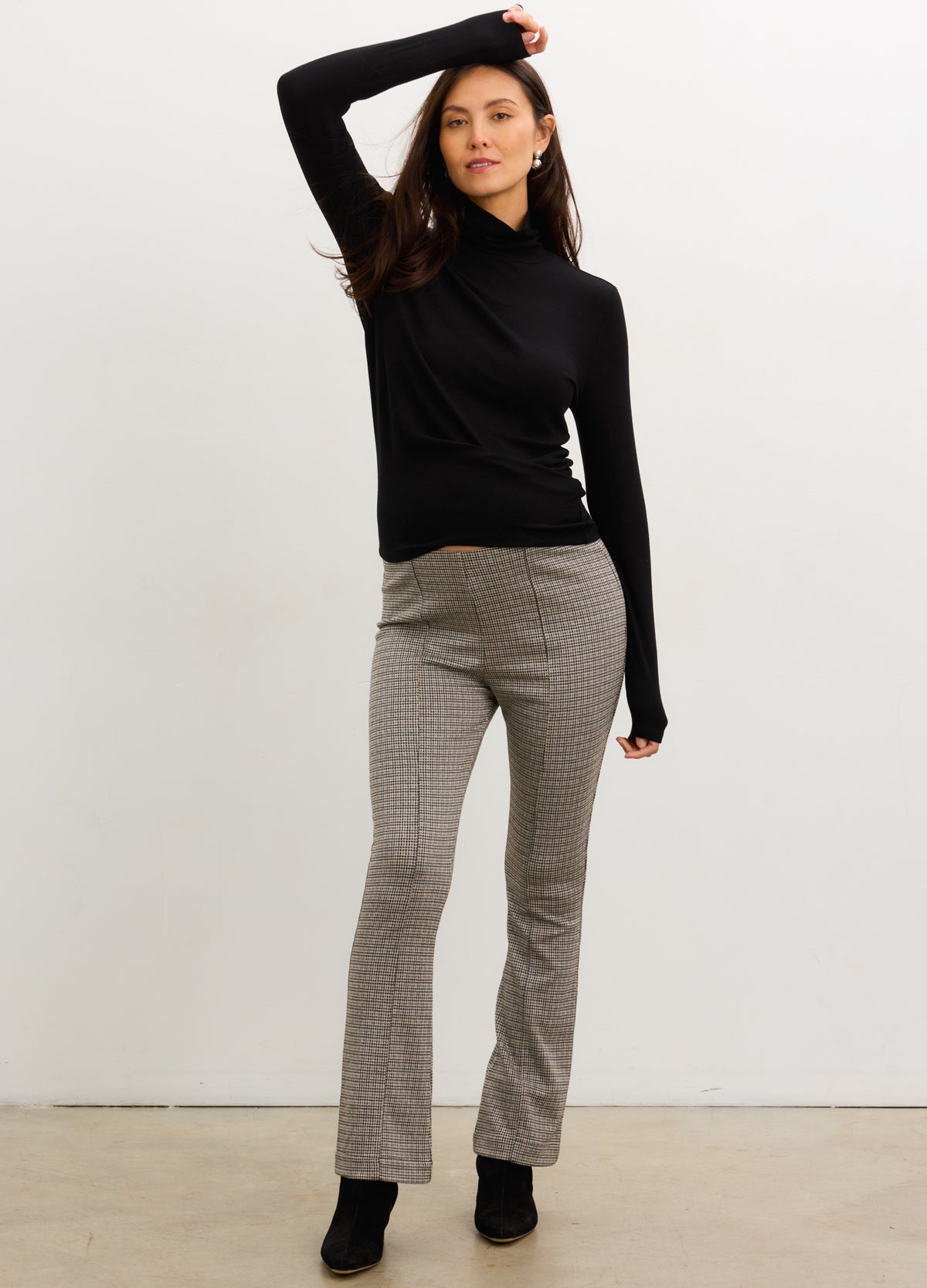 Pregnant woman wearing a black turtleneck and gray checkered pants against a white background