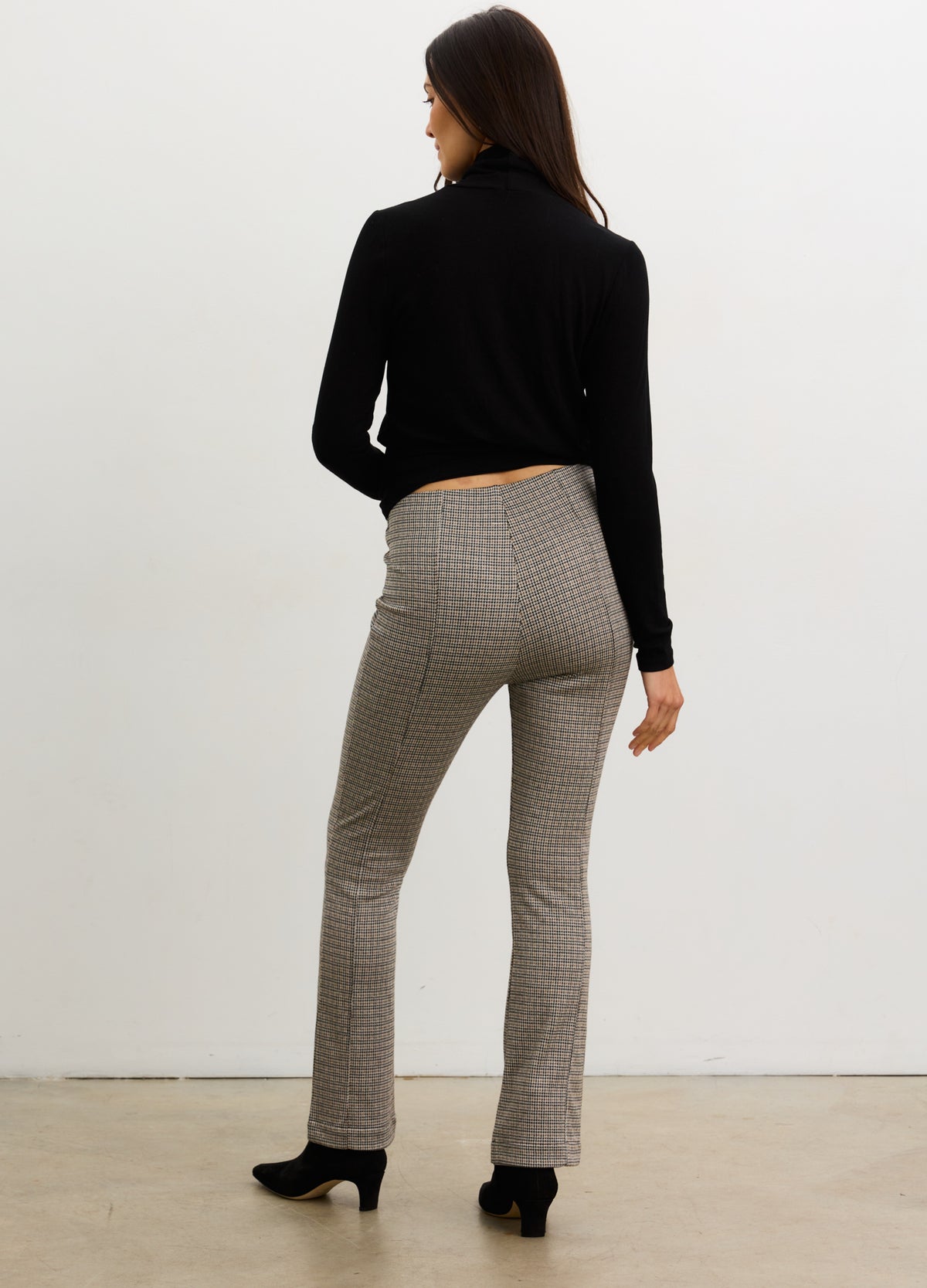 Pregnant woman wearing a black top and gray checkered pants against a white background