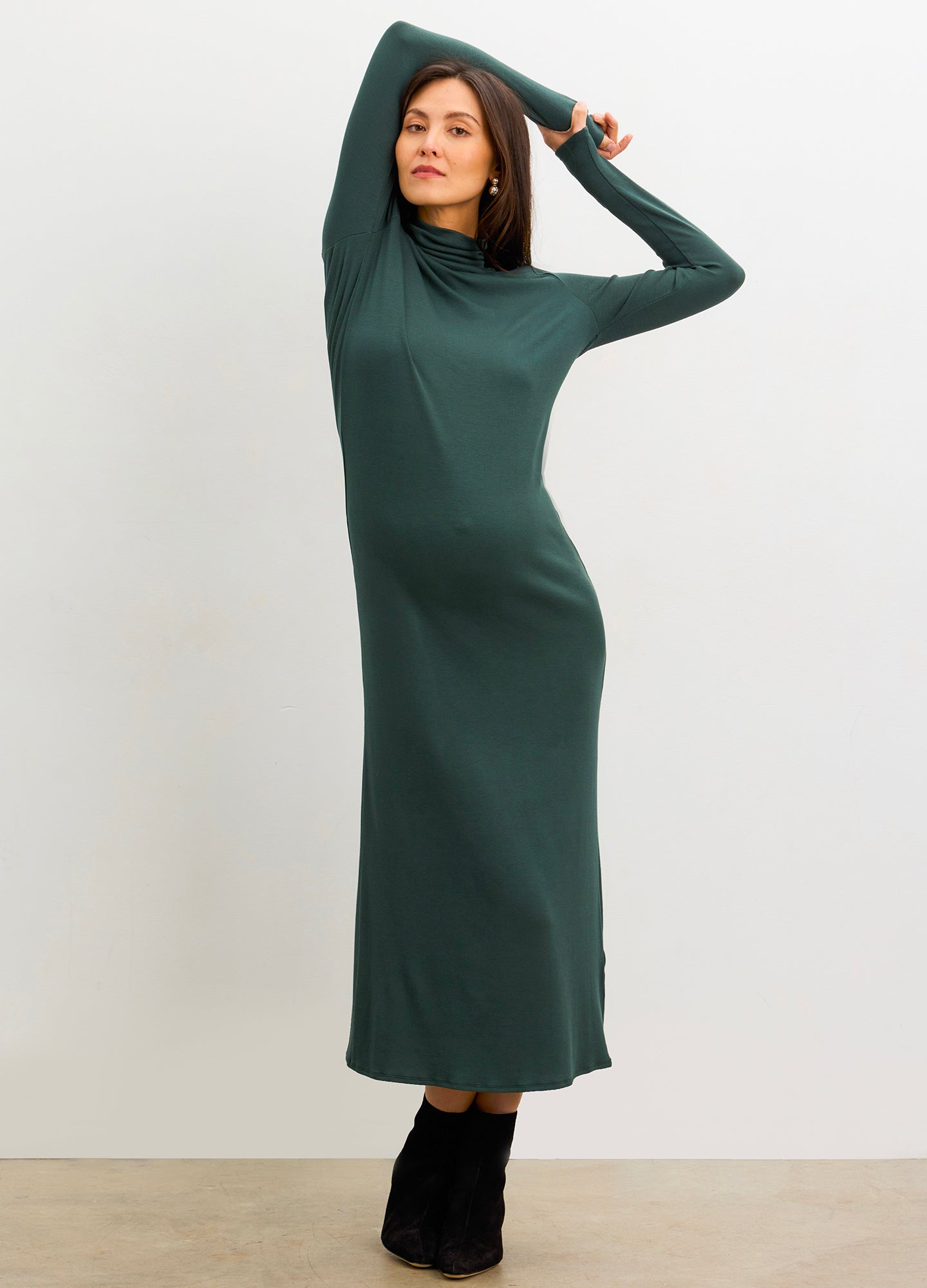 Pregnant woman wearing a green dress with long sleeves against a white background