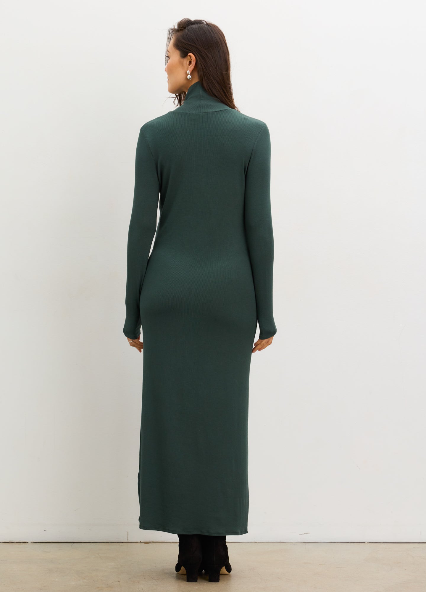 Pregnant woman wearing a green dress with long sleeves against a white background