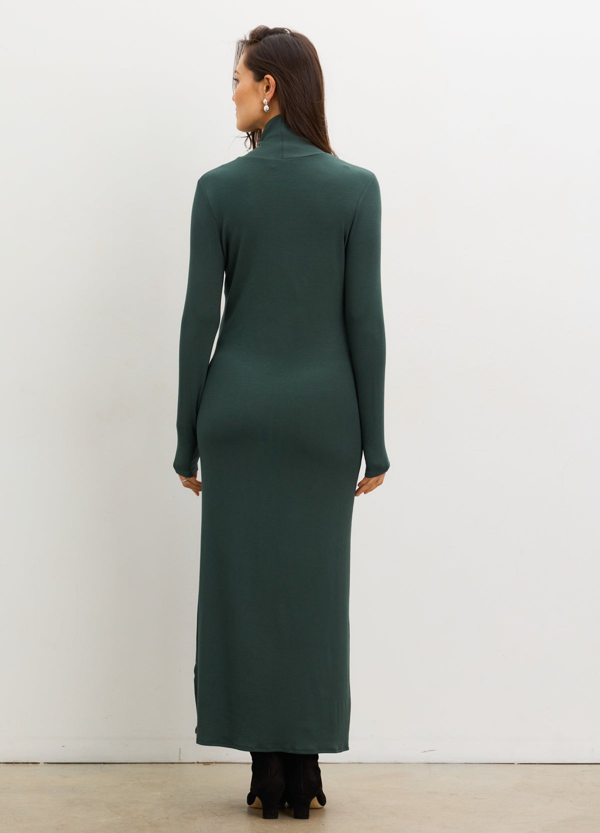 Pregnant woman wearing a green dress with long sleeves against a white background