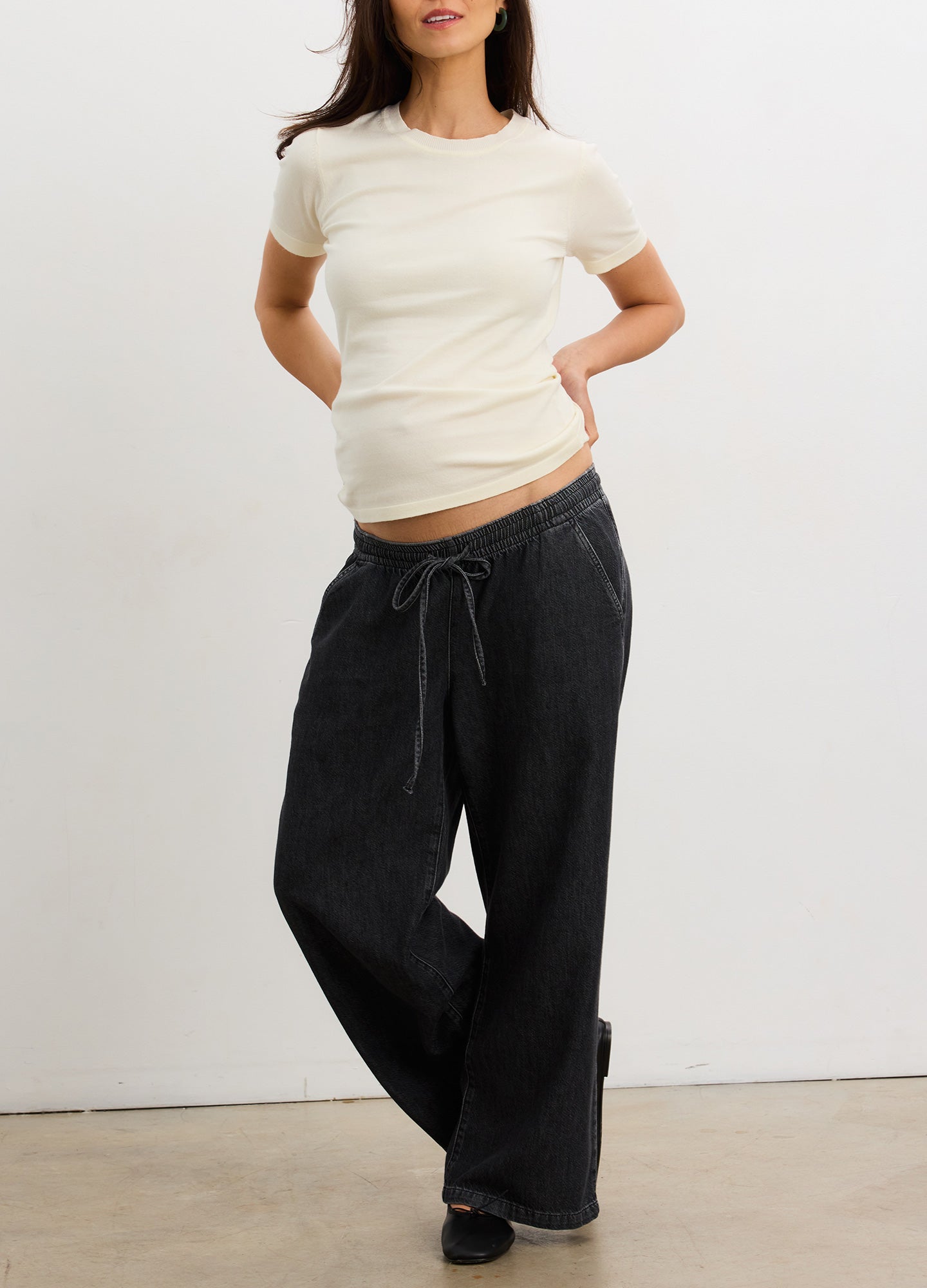 Cream-colored short-sleeve maternity knit tee with a fitted silhouette, paired with loose black drawstring pants.