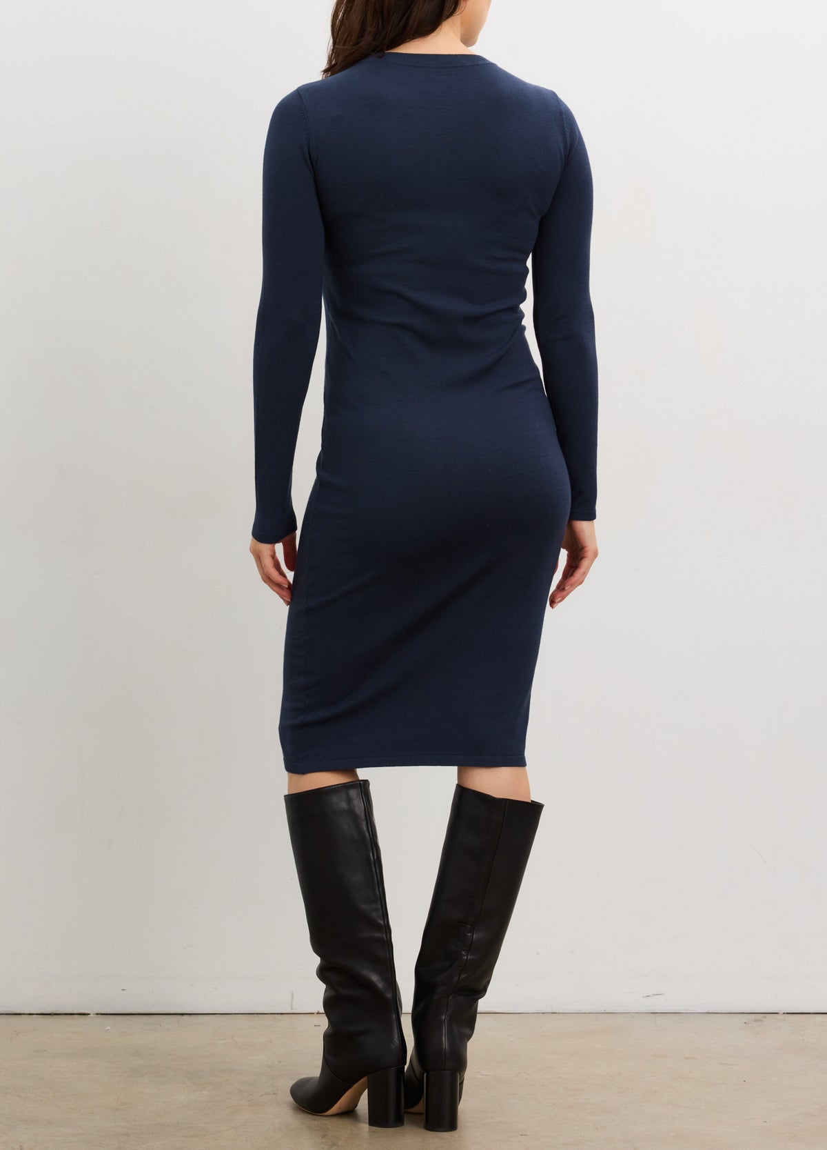 Navy blue knit midi dress with long sleeves and bodycon fit, styled for maternity, paired with black knee-high boots.