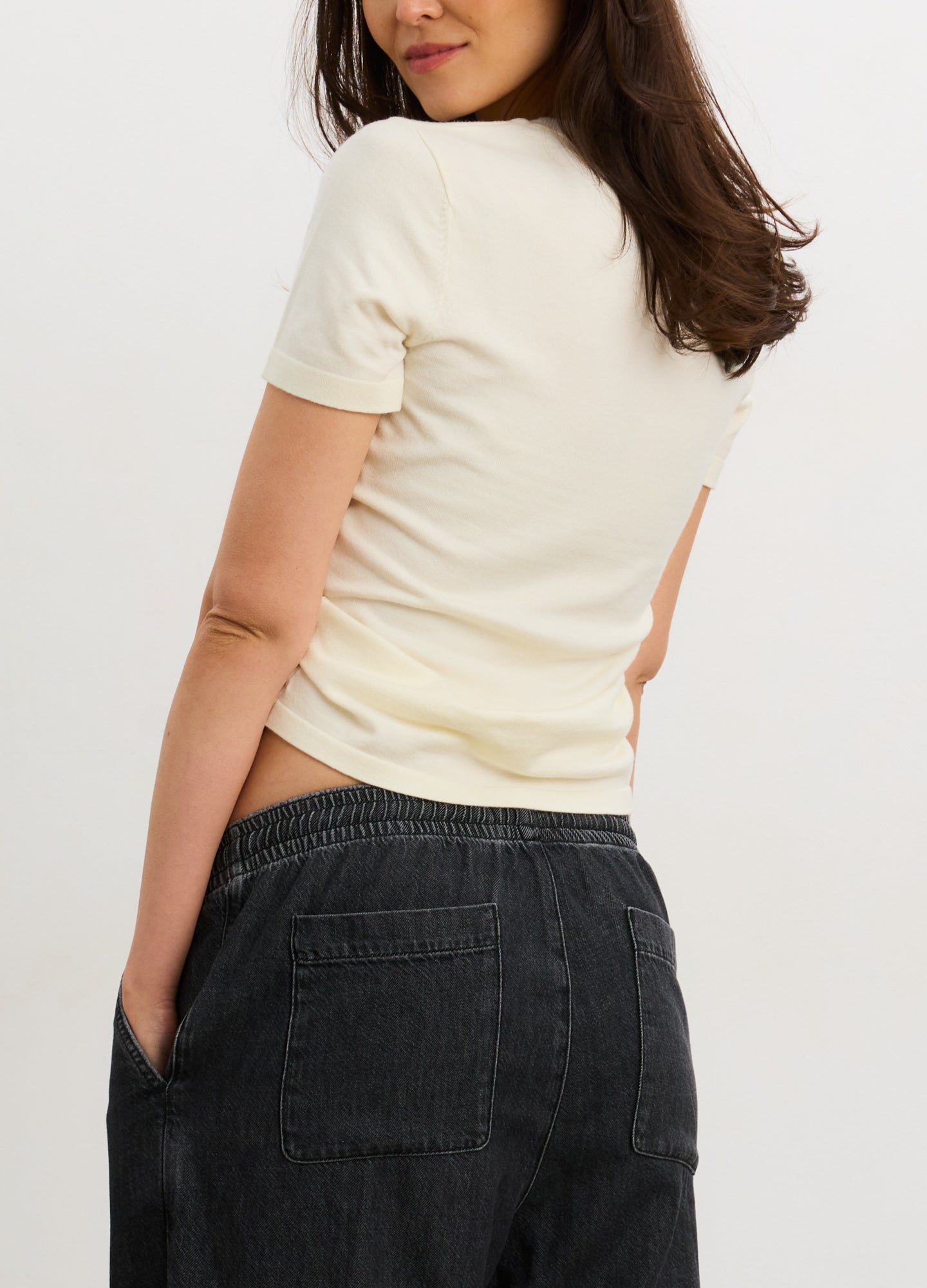 Cream-colored fitted knit tee with short sleeves, designed to contour a pregnant belly, paired with dark denim jeans.