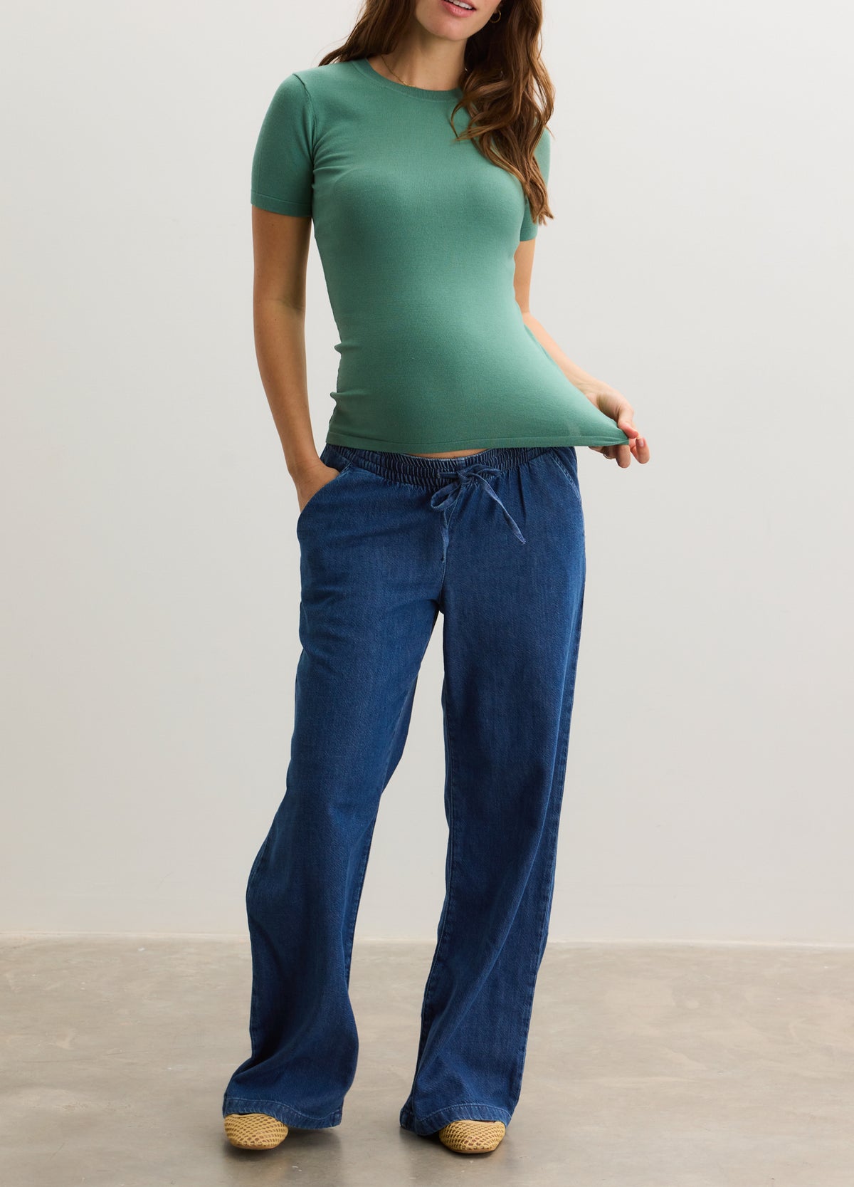 Maternity green soft knit short-sleeve tee paired with loose dark blue drawstring pants.