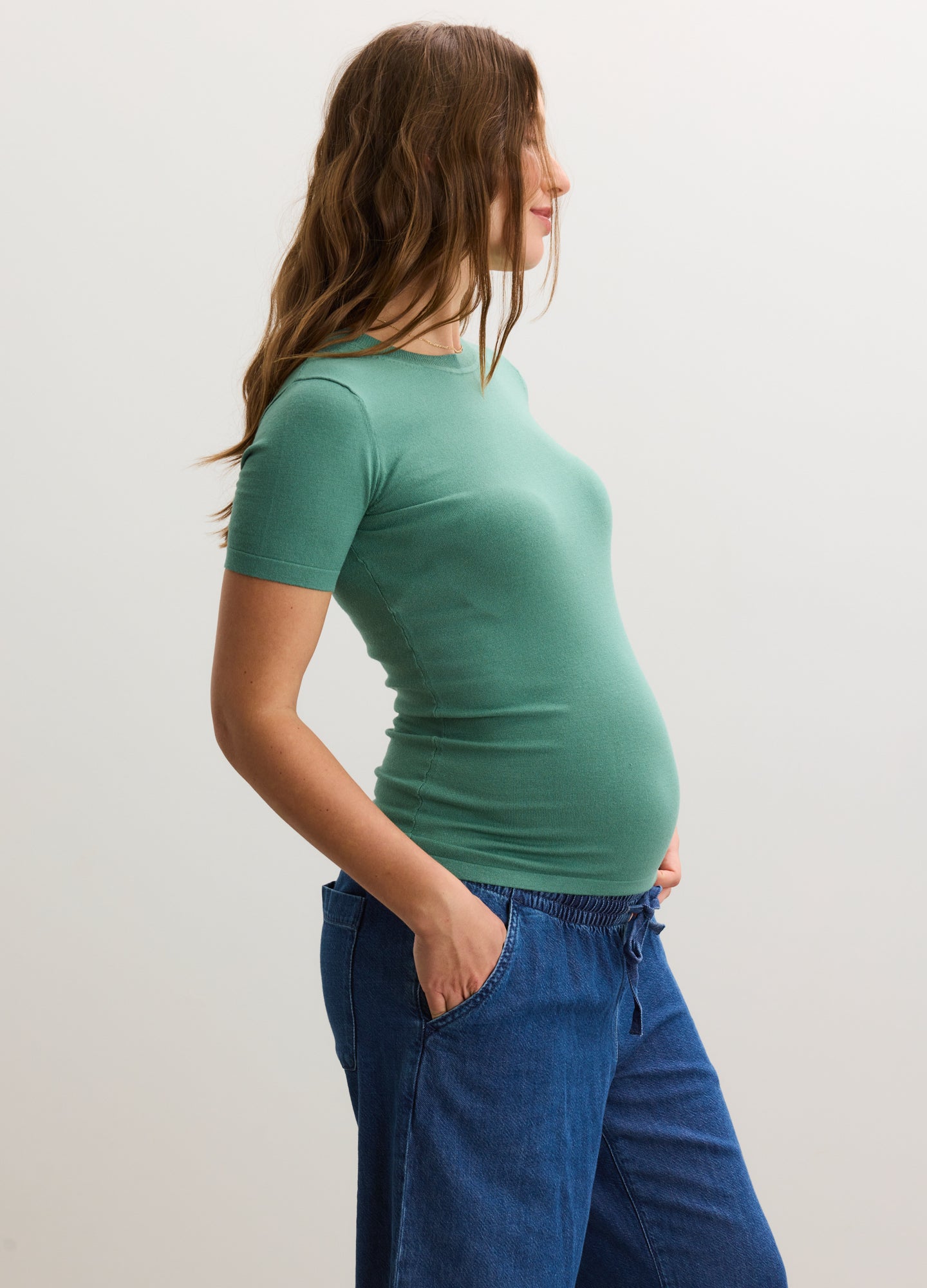 Green short-sleeve knit maternity tee with a fitted silhouette, styled on a pregnant model.