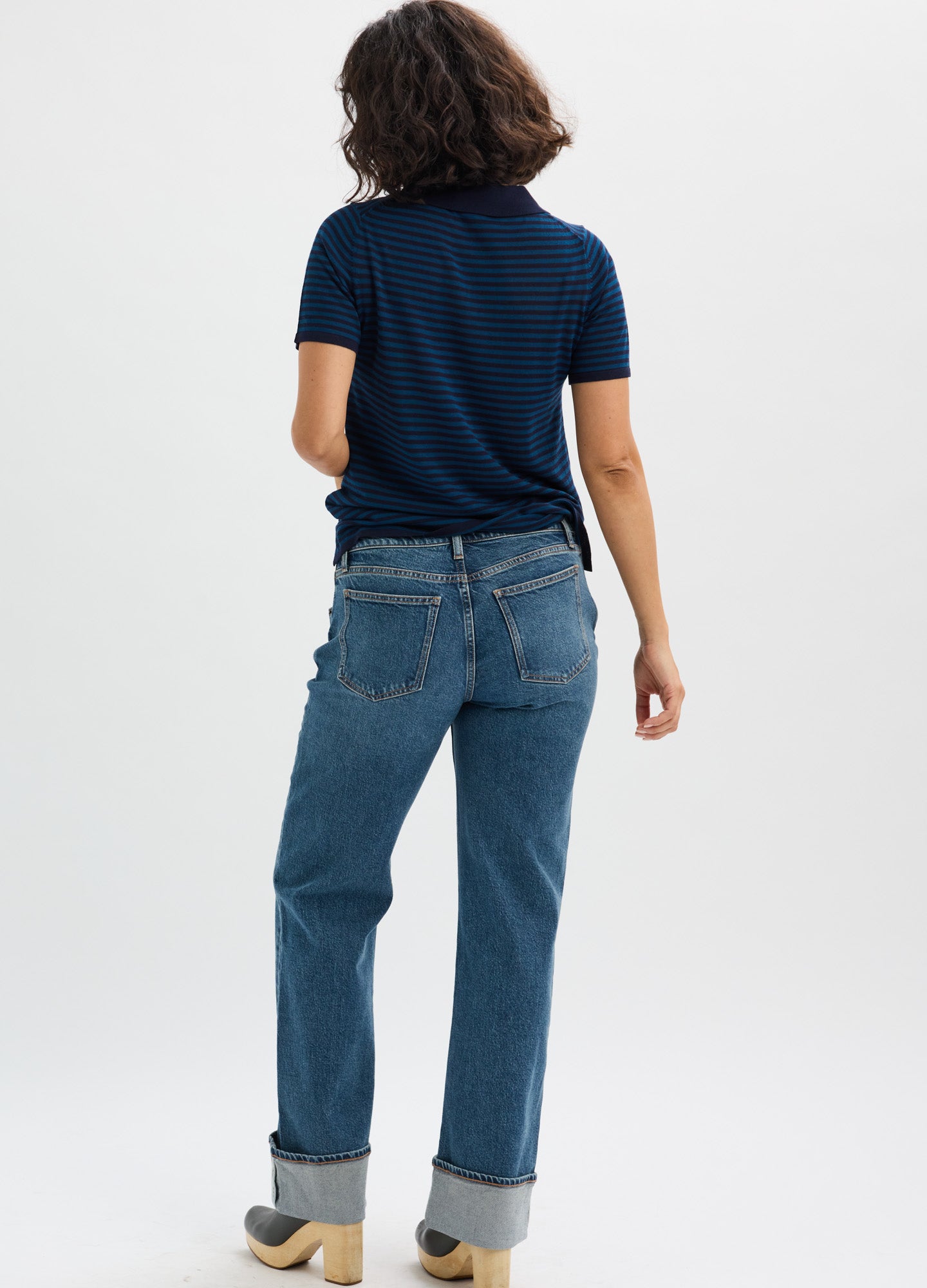 Navy blue short-sleeve maternity shirt paired with cuffed medium-wash jeans on a pregnant model viewed from behind.
