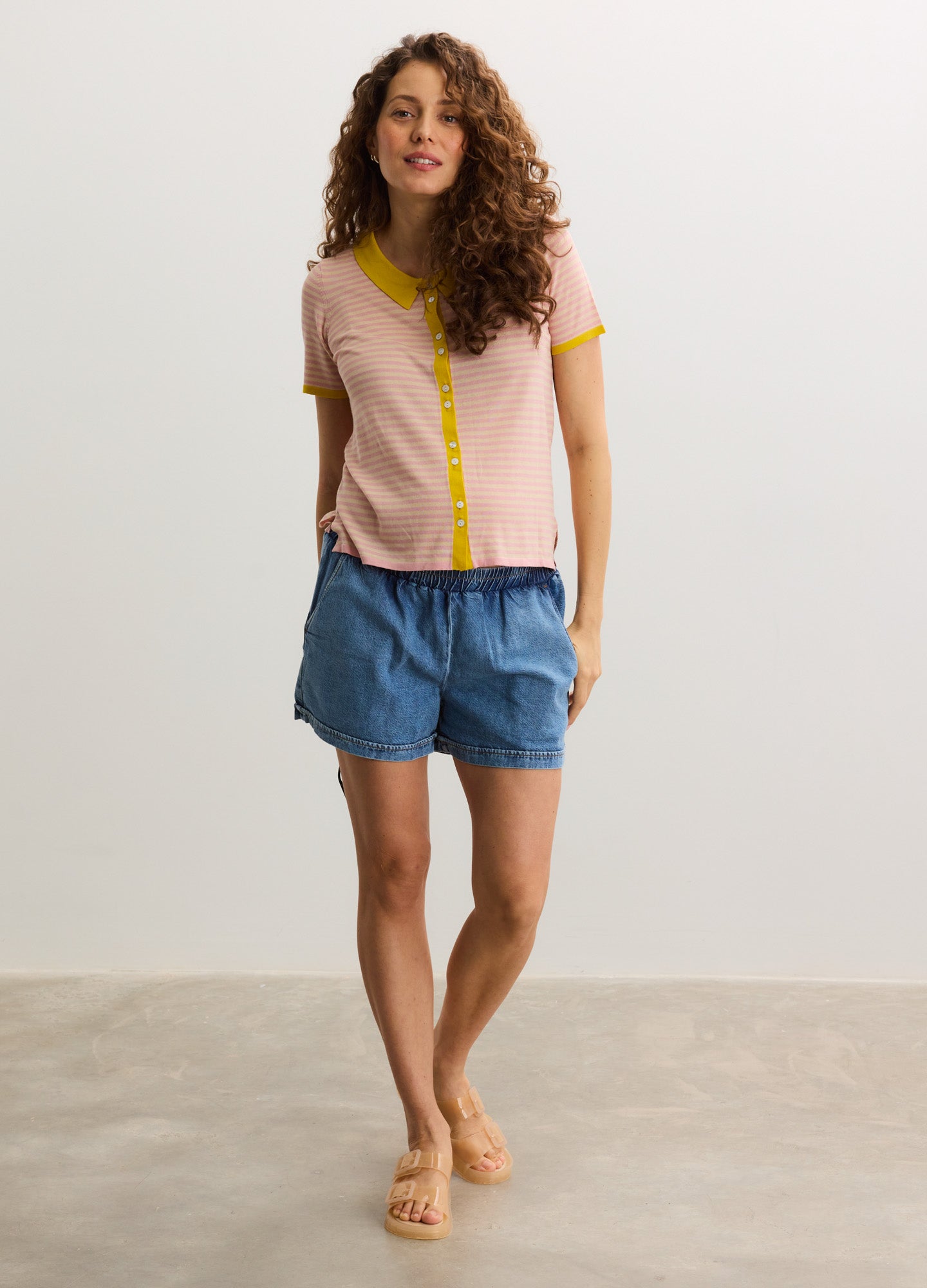 Light pink short-sleeve maternity shirt with yellow trim and buttons, paired with loose blue shorts.