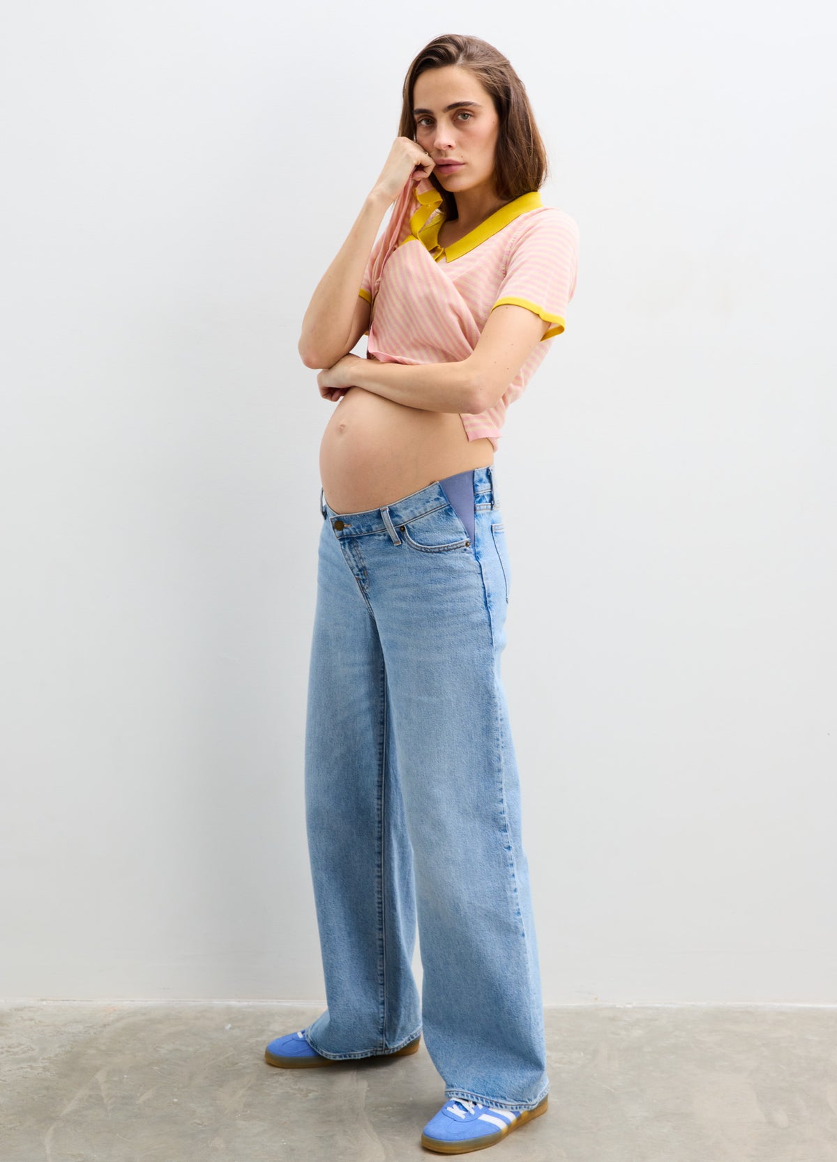 Light pink maternity shirt with yellow trim, short sleeves, ribbed knit, paired with wide-leg blue jeans and white sneakers.