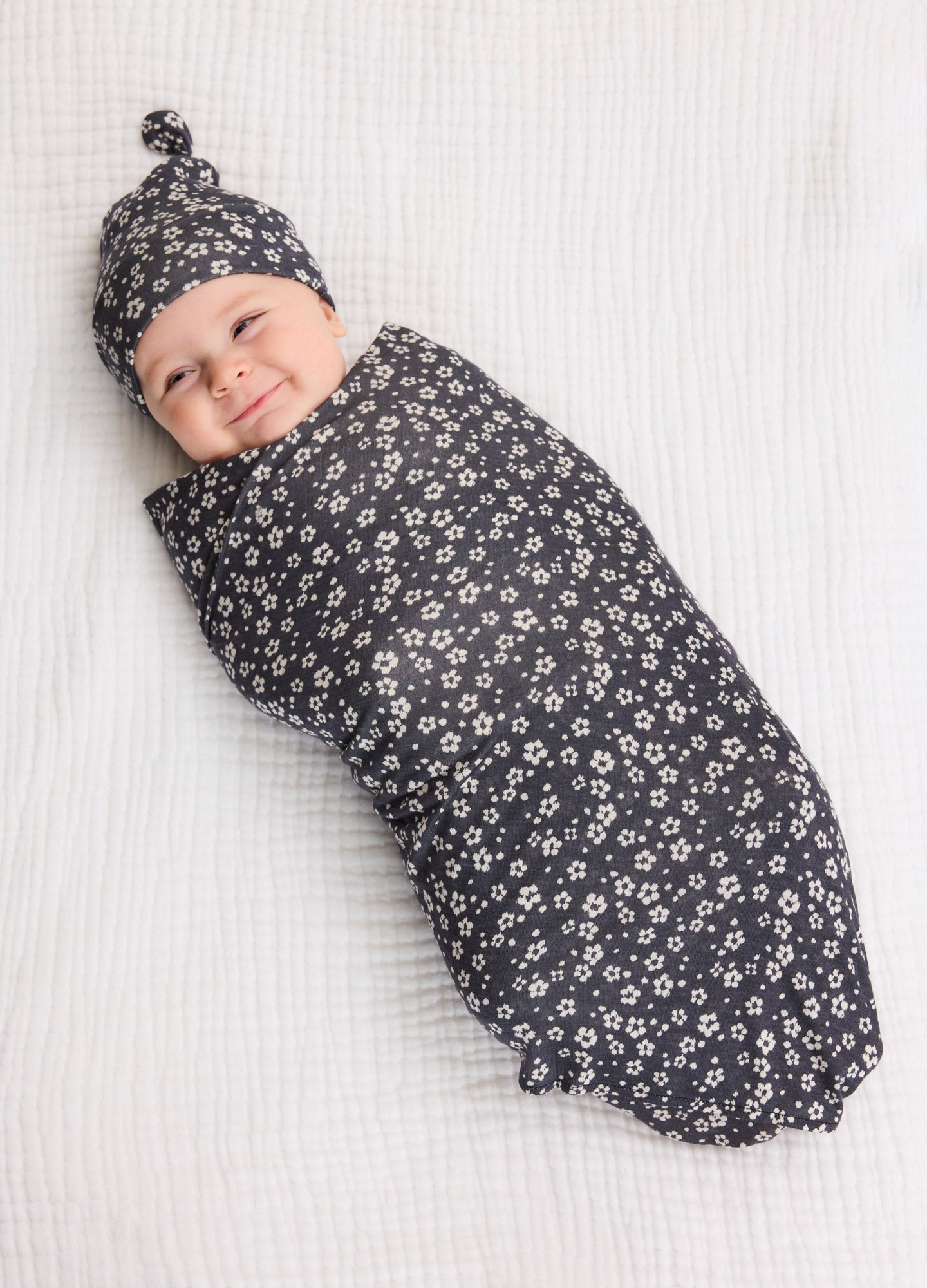 Dark gray baby swaddle and matching knotted hat with white floral pattern on soft fabric.
