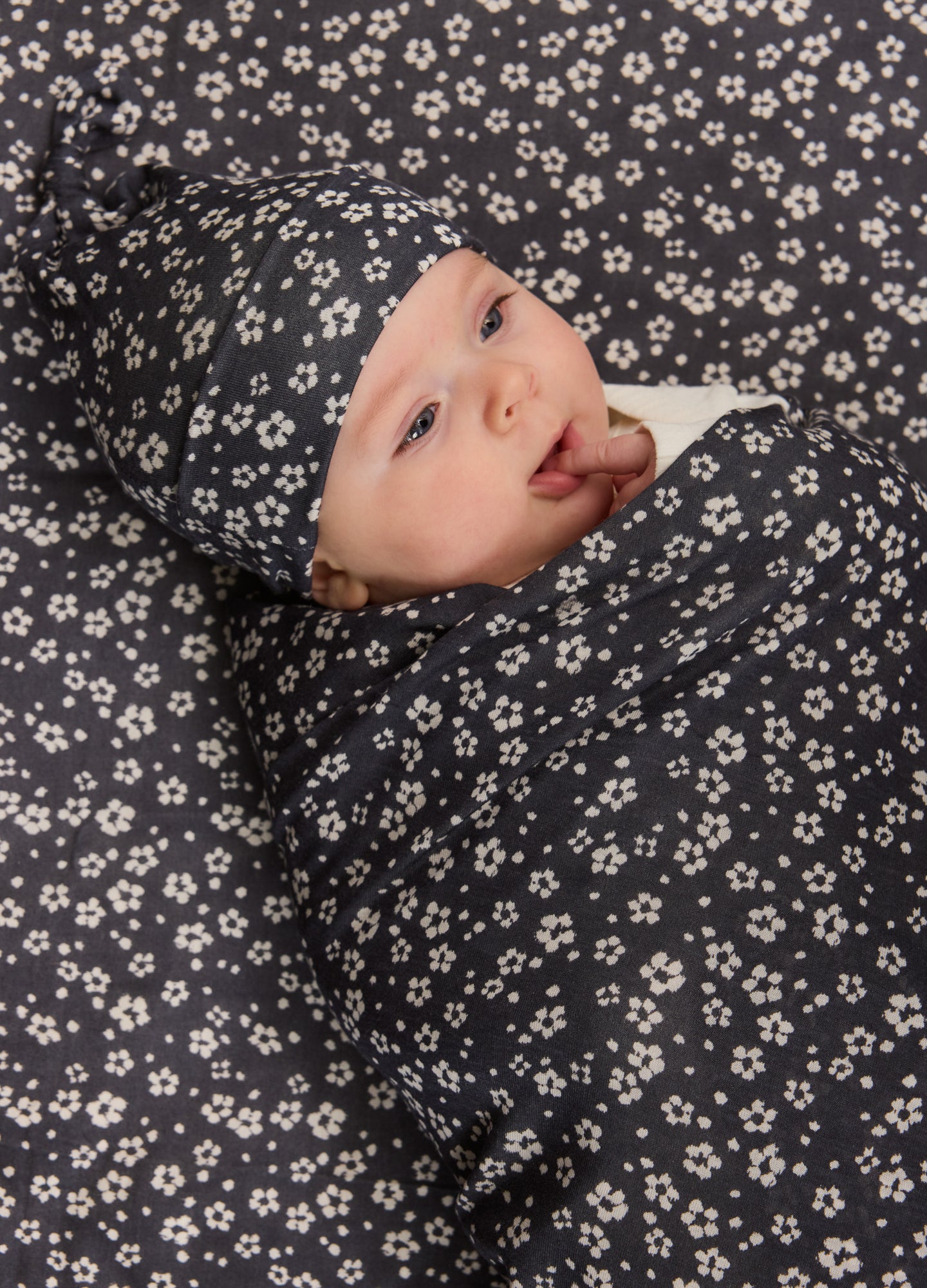 Black baby swaddle and matching hat with small white flower pattern on soft fabric.