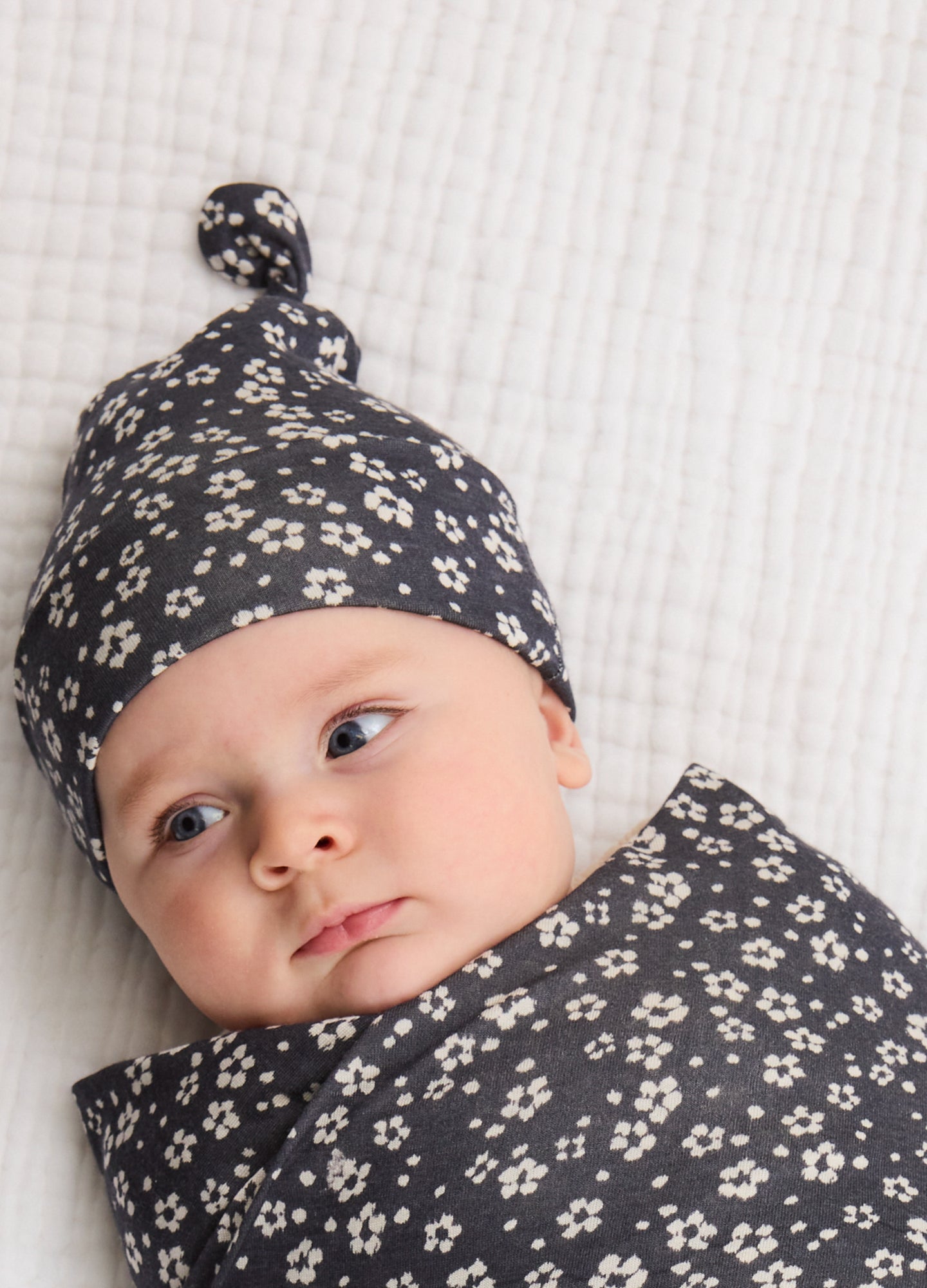 Black baby swaddle hat and matching swaddle blanket with small white floral print, soft fabric, knotted top on hat.