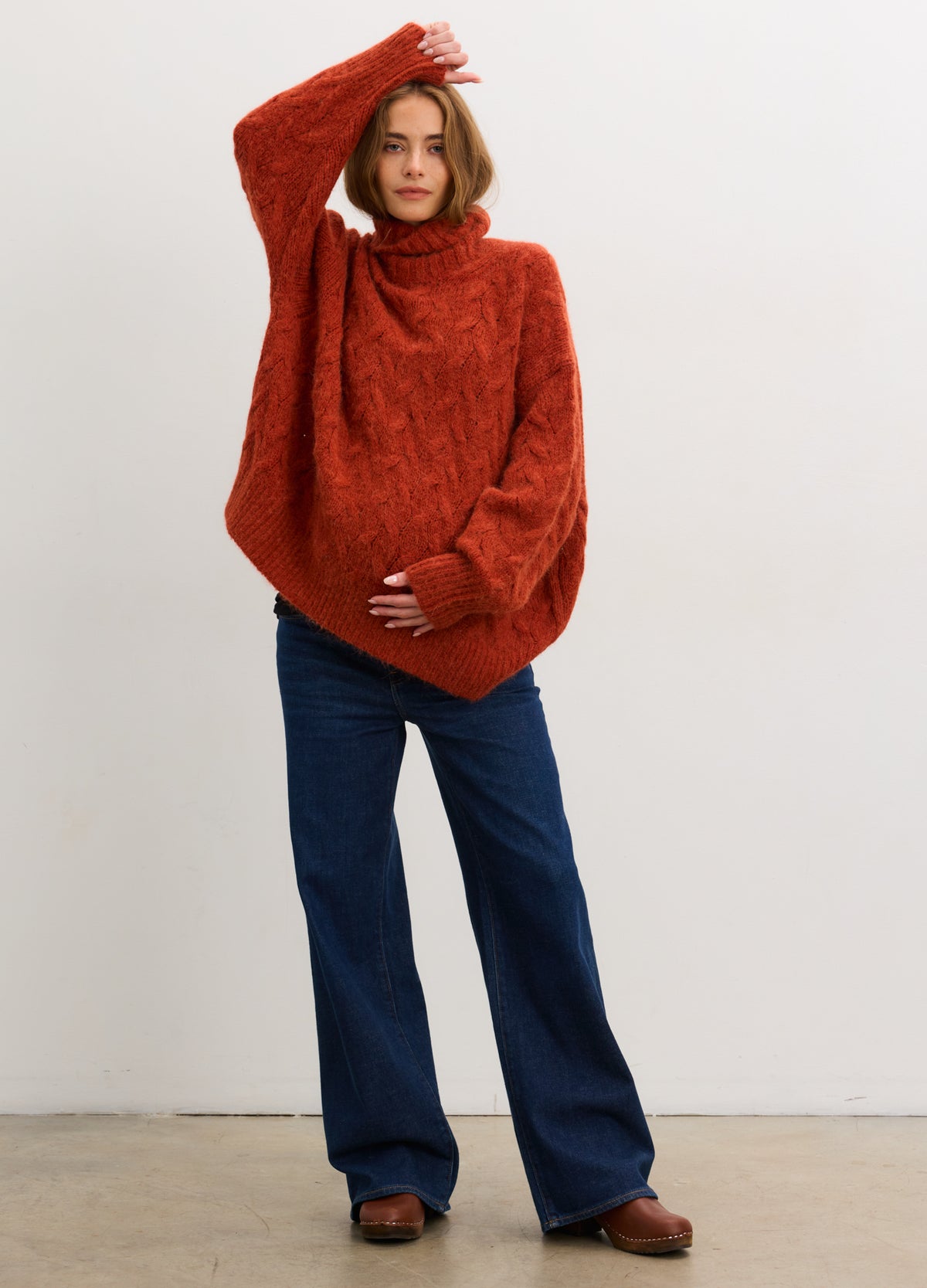 Rust-colored cable-knit alpaca turtleneck sweater paired with dark blue wide-leg pants.