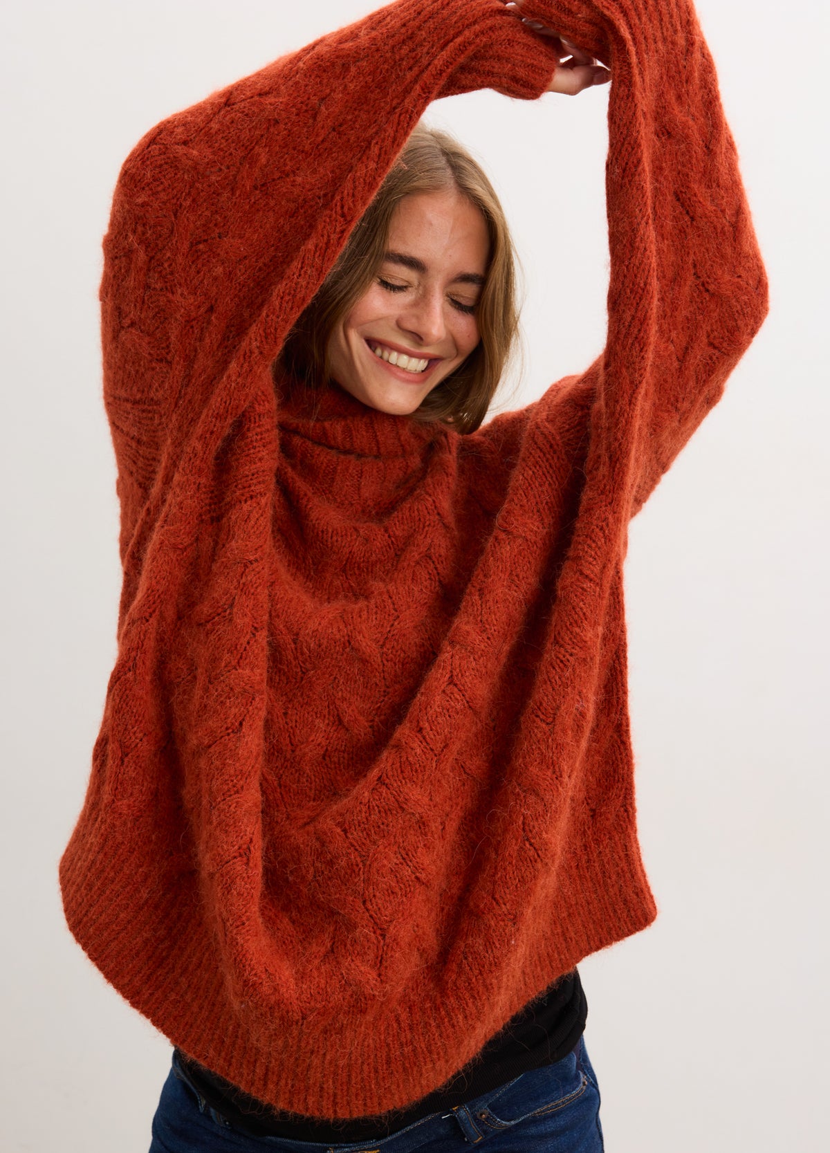 Rust-colored alpaca cable knit turtleneck sweater styled for maternity with relaxed fit and long sleeves.