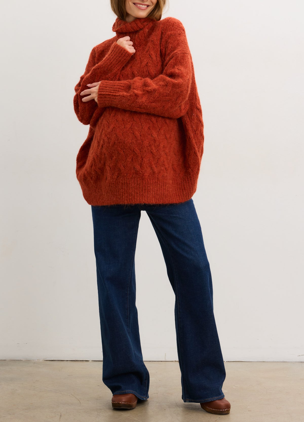 Rust-colored cable knit alpaca turtleneck sweater styled for maternity with long sleeves and relaxed fit.