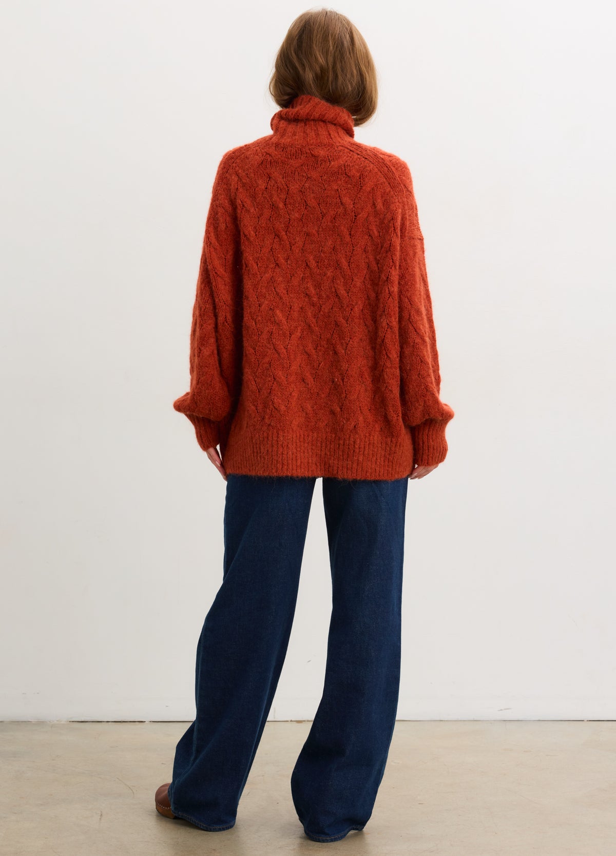 Rust-colored alpaca cable-knit turtleneck sweater with relaxed fit and long sleeves.