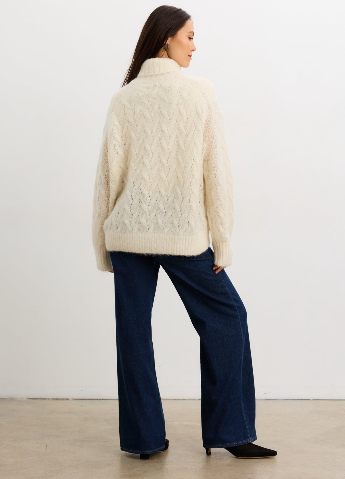Cream cable-knit alpaca turtleneck sweater with a relaxed fit, worn over navy wide-leg pants.