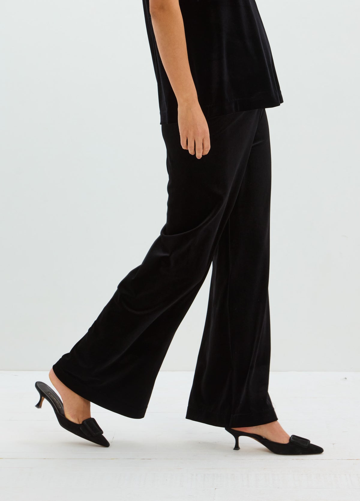 Black stretch velvet pants with a smooth finish, relaxed straight legs, and a subtle flare at the hem.