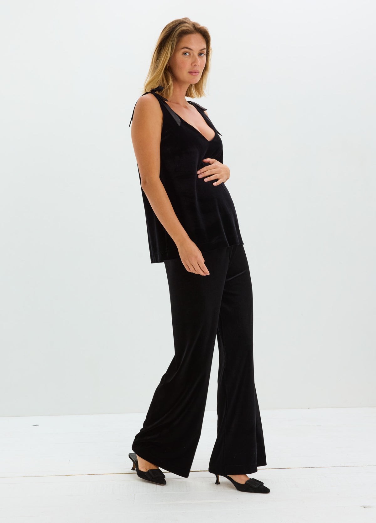 Black stretch velvet pants with a subtle sheen and wide, flowing legs, styled with a sleeveless black top.