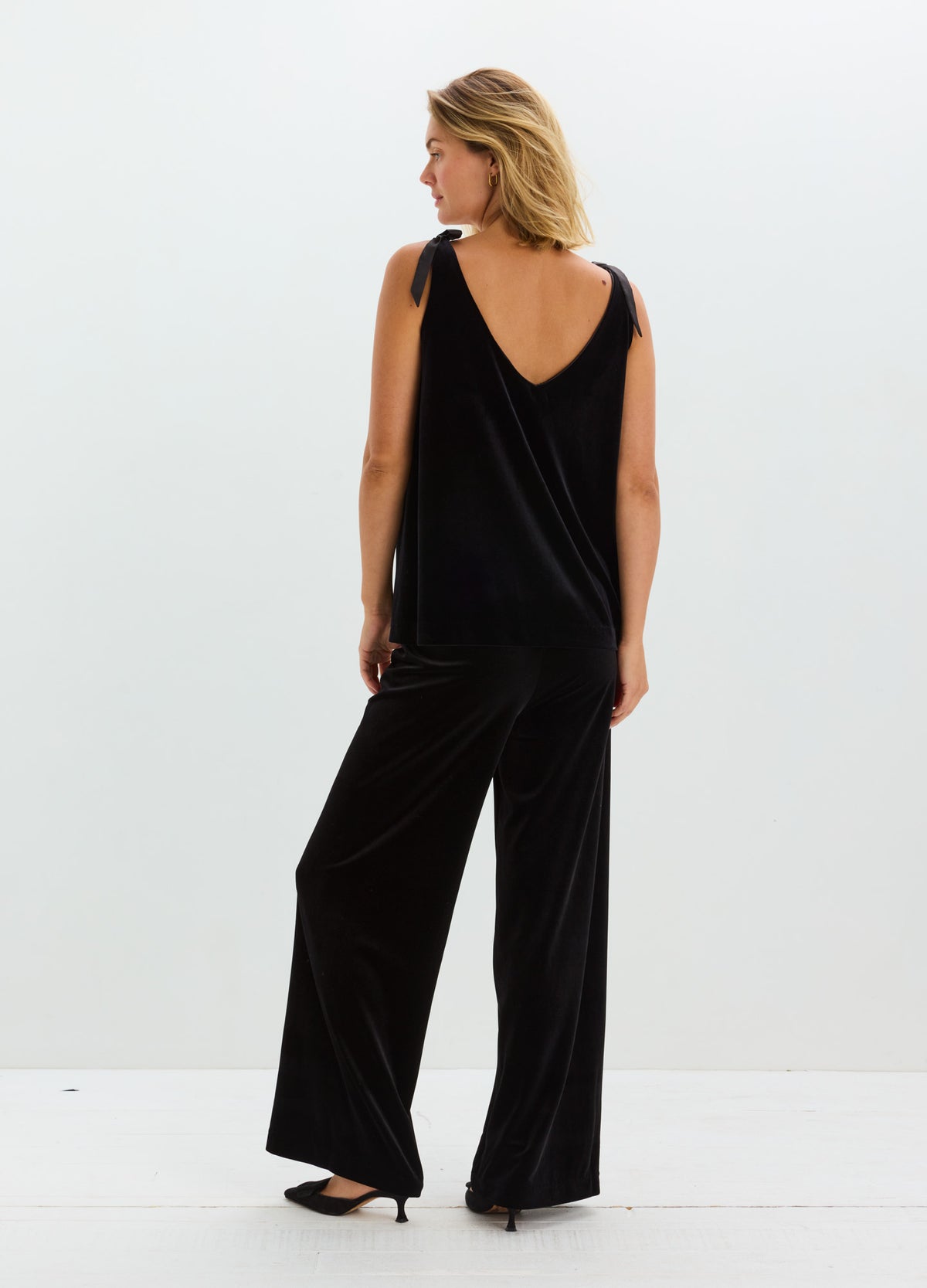 Black stretch velvet wide-leg pants with a soft sheen, modeled with a sleeveless black top.