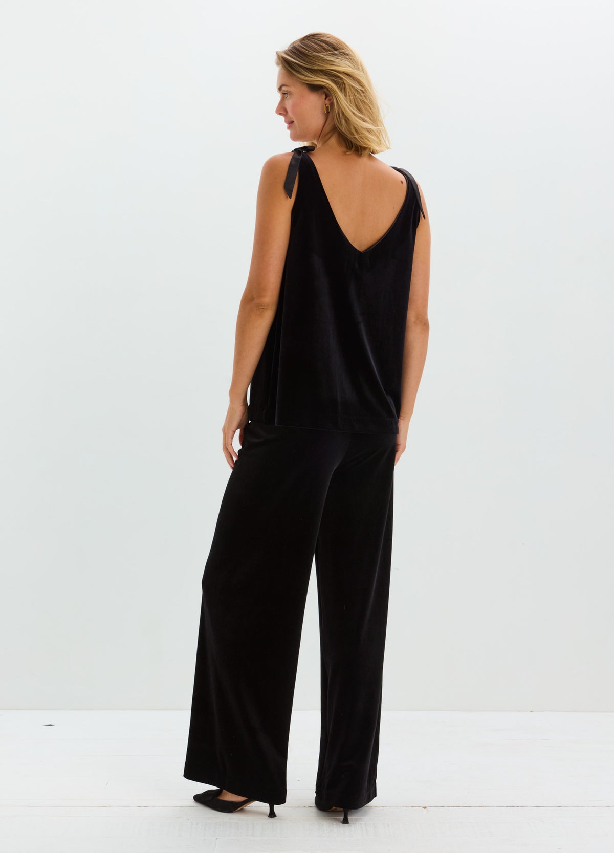 Black stretch velvet sleeveless top with a deep V-back, paired with wide-leg black trousers.