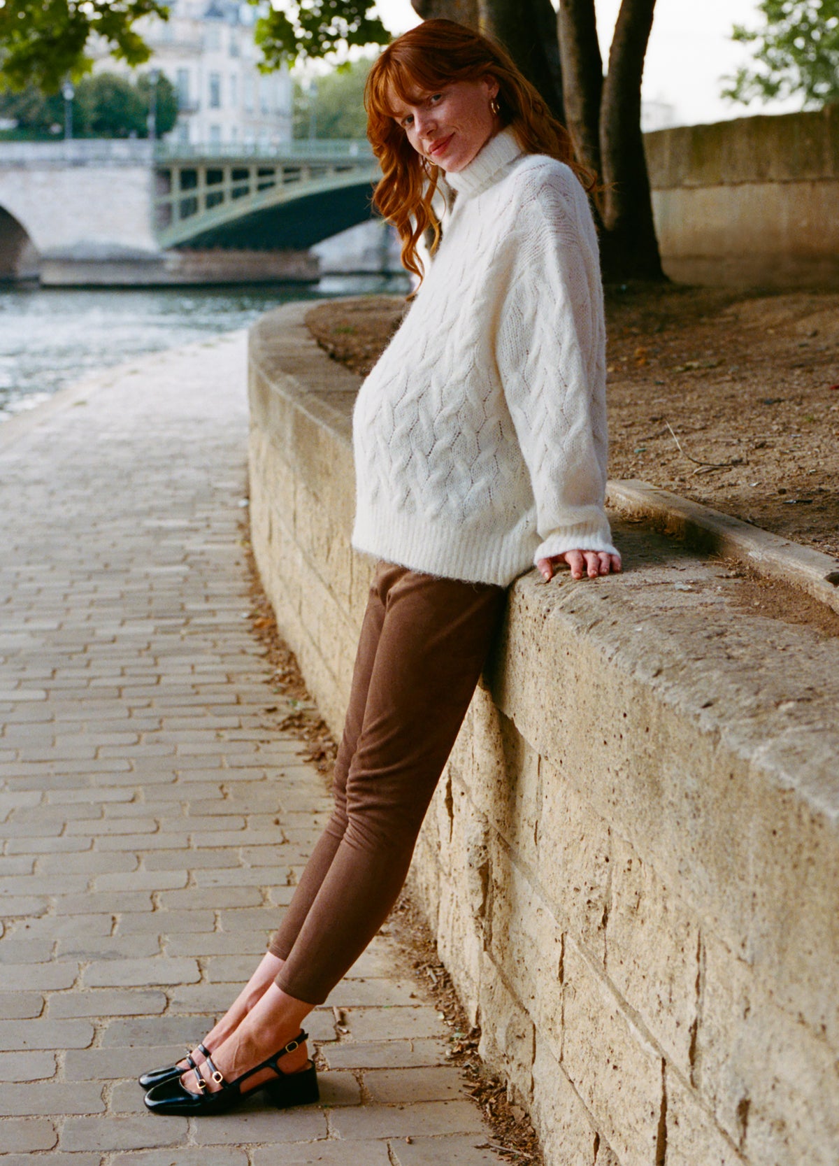 Brown stretch suede maternity leggings worn by a pregnant woman with a cozy white cable-knit sweater and black sandals by a.