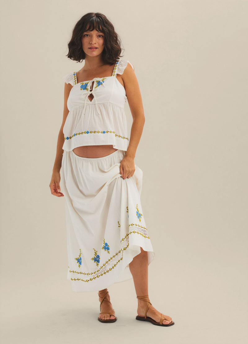 White maternity skirt with blue and gold embroidery along the hem, flowing lightweight fabric, mid-calf length.