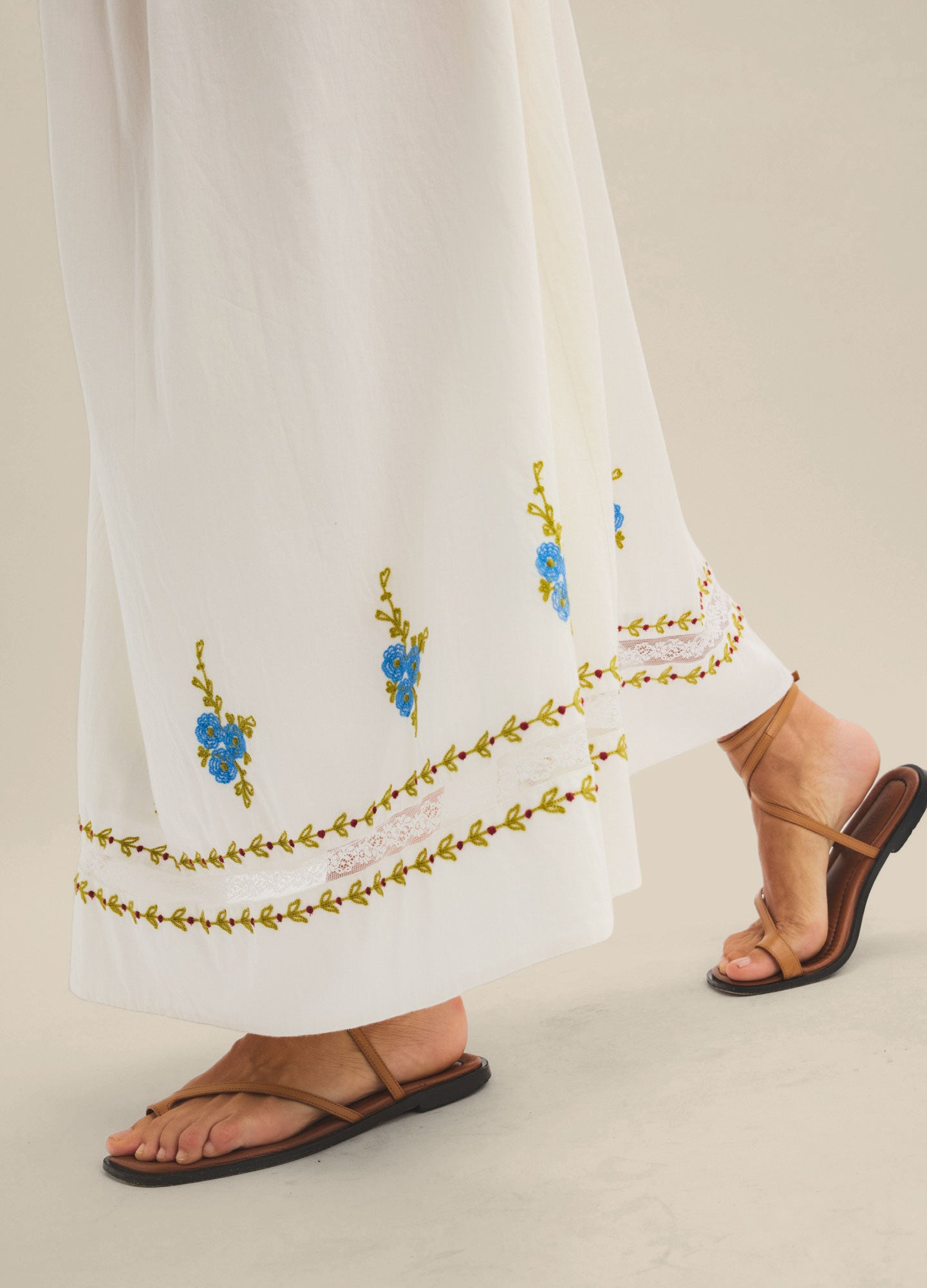 White maternity skirt with blue floral embroidery and decorative trim at the hem, flowing fit.