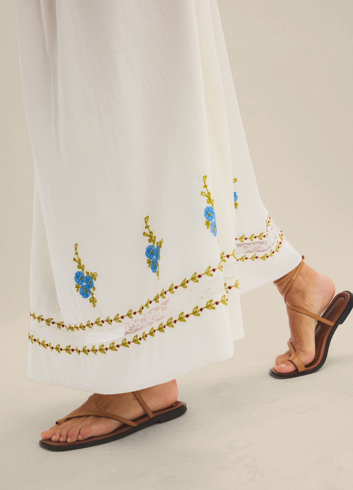 White maternity skirt with blue floral embroidery and decorative trim at the hem, flowing fit.