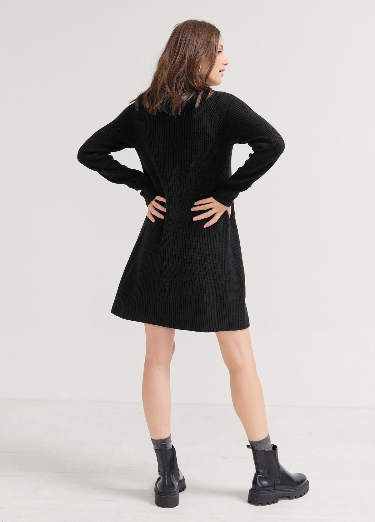 Black knitted mini sweater dress with long sleeves, maternity fit ideal for pregnant women, paired with black ankle boots.