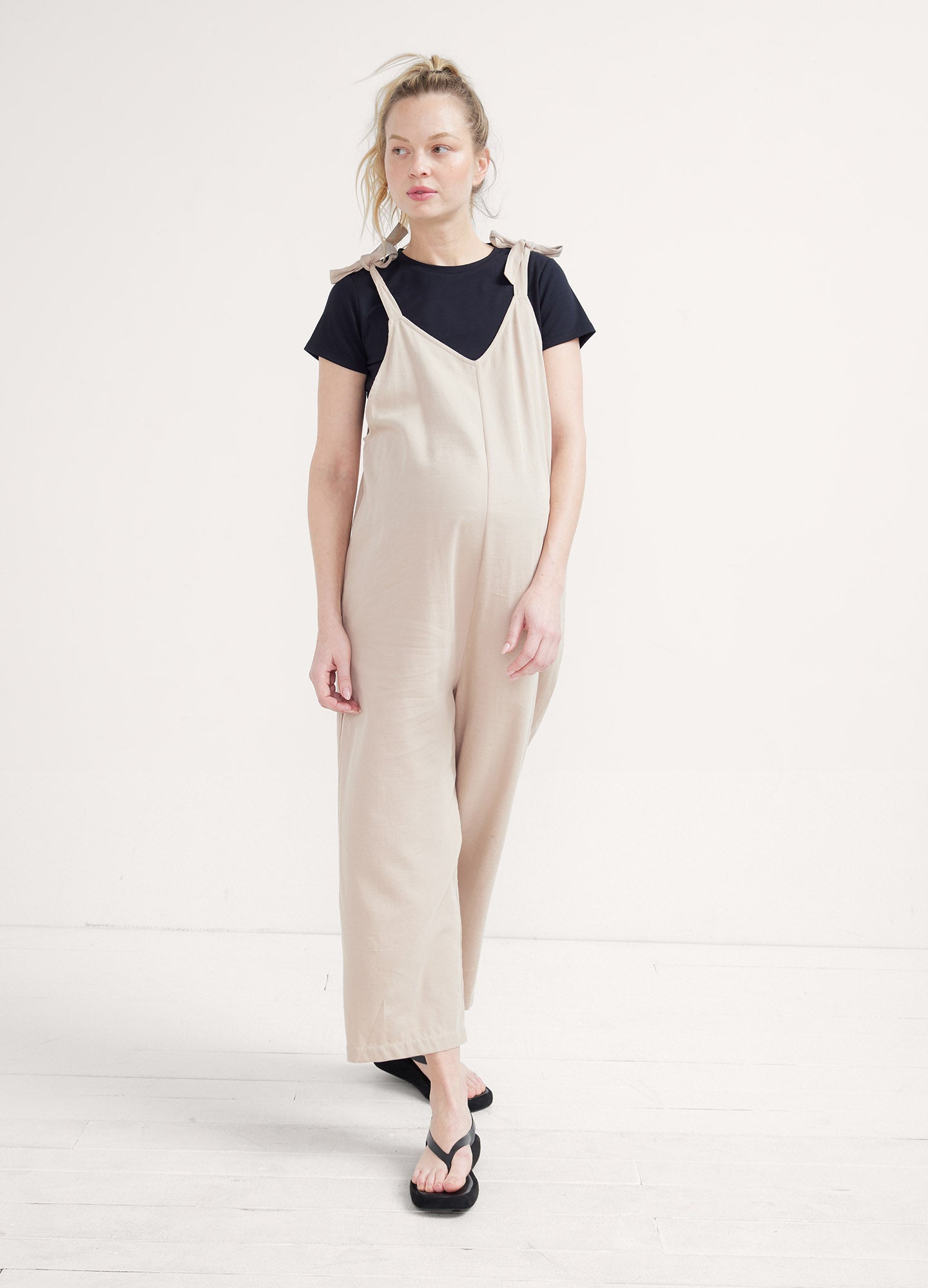 Beige sleeveless maternity jumpsuit with wide legs, worn over a black short-sleeve top.
