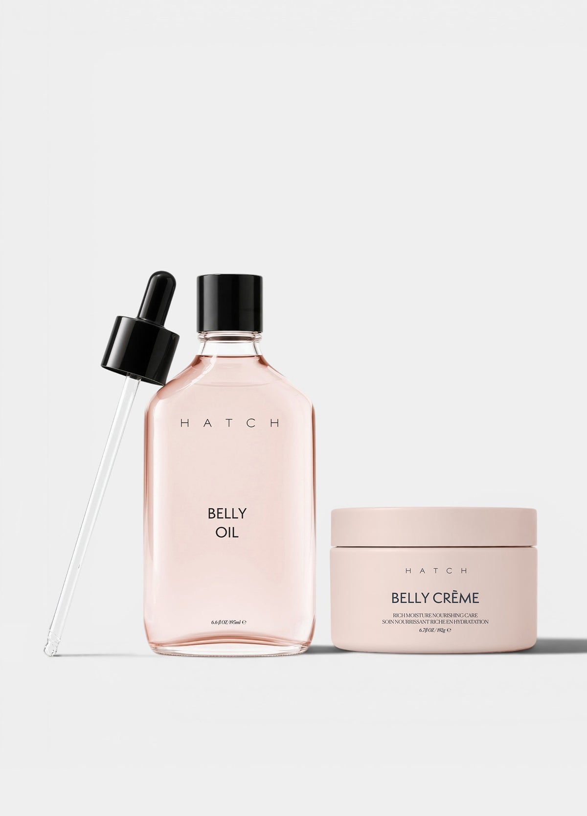 Clear glass bottle with pale pink belly oil and black dropper beside matching light pink belly cream in a round jar.