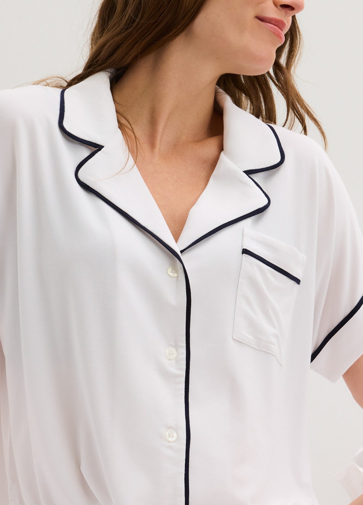 White short-sleeve maternity pajama top with black piping and button closure, soft jersey fabric.