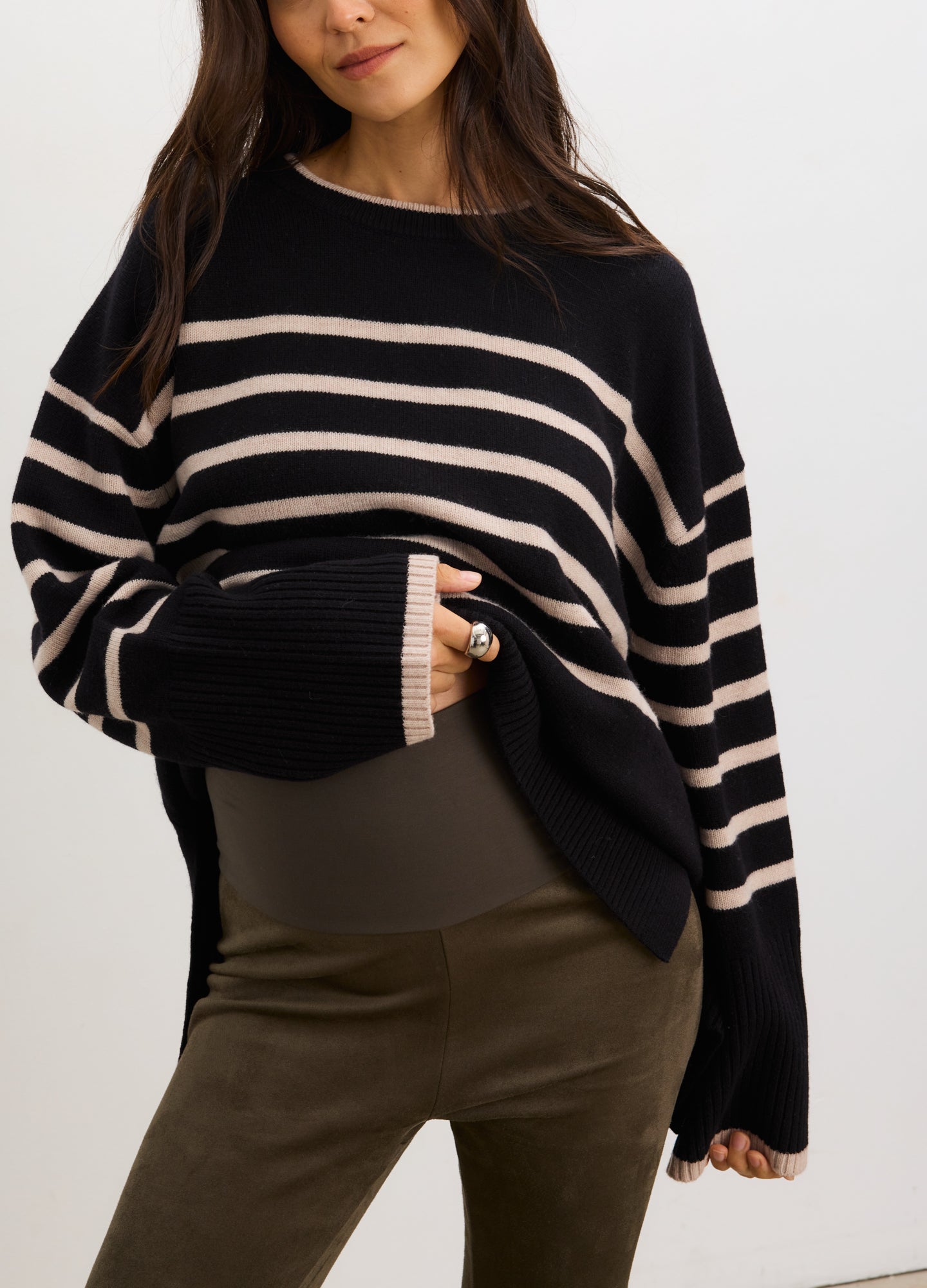 Pregnant woman wearing a navy and beige striped sweater and green pants against a white background