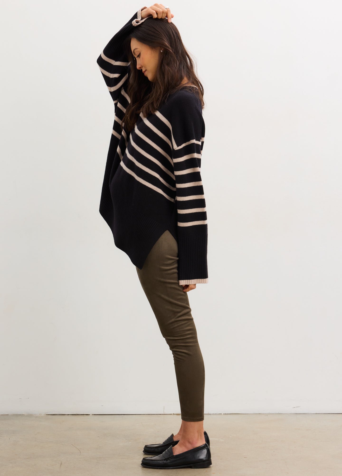 Pregnant woman wearing a navy and beige striped sweater and green pants against a white background
