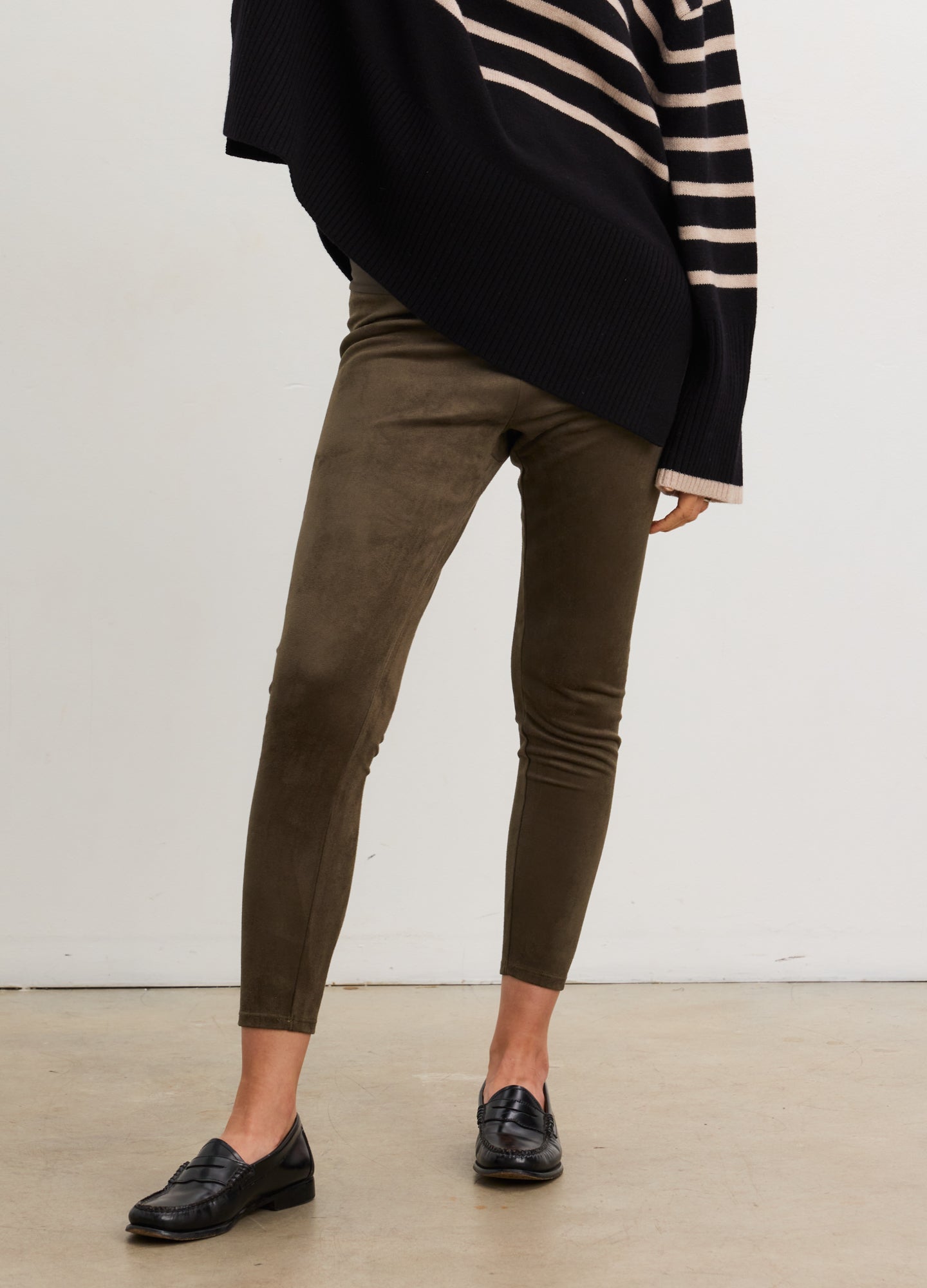 Pregnant woman wearing a navy and beige striped sweater and green pants against a white background